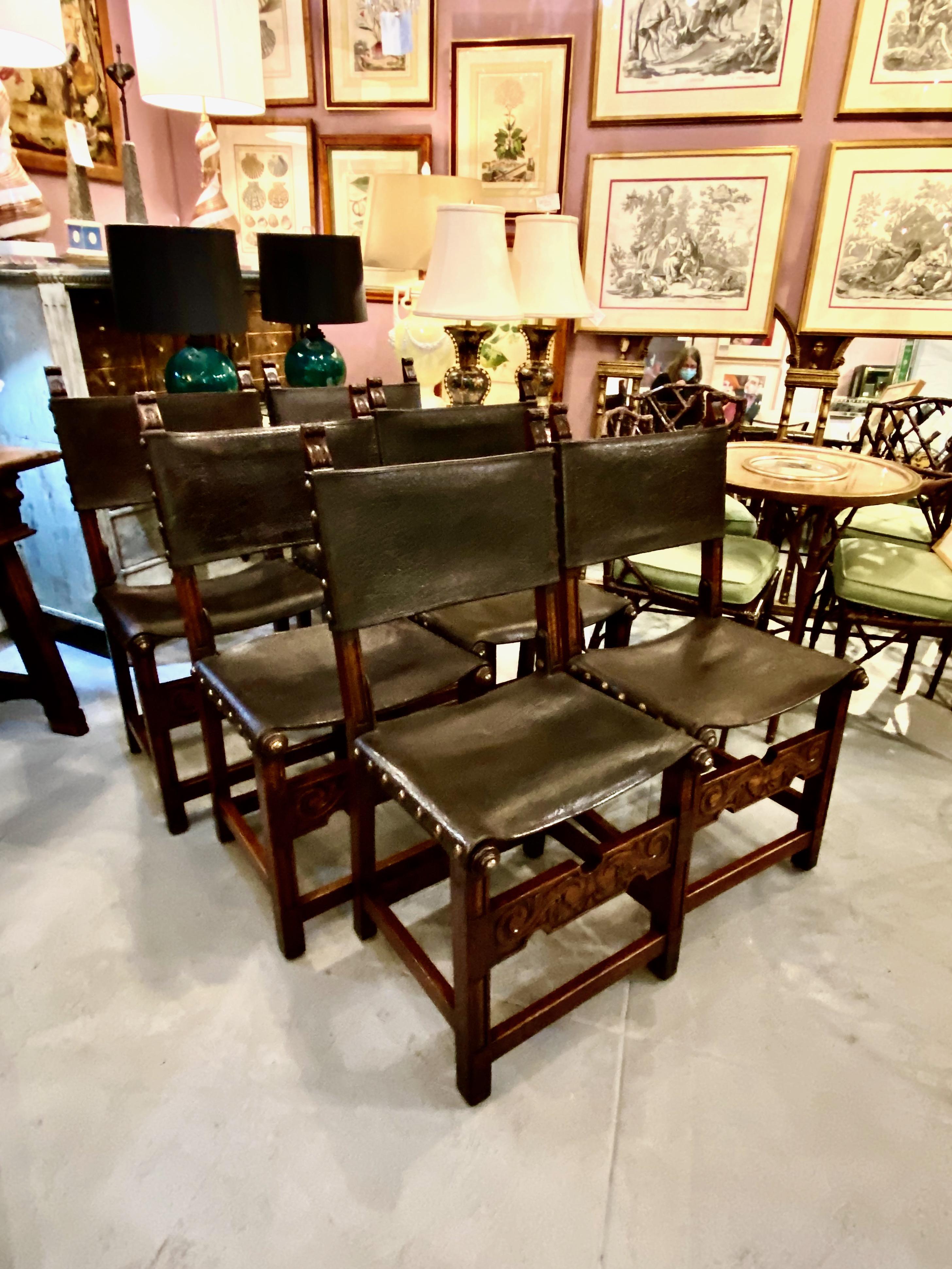 This is an unusual set of six antique Spanish early 20th century carved oak and saddle leather dining chairs. The chairs appear to be in original condition--the leather is very sturdy and has acquired a desirable deep natural patina. The large brass