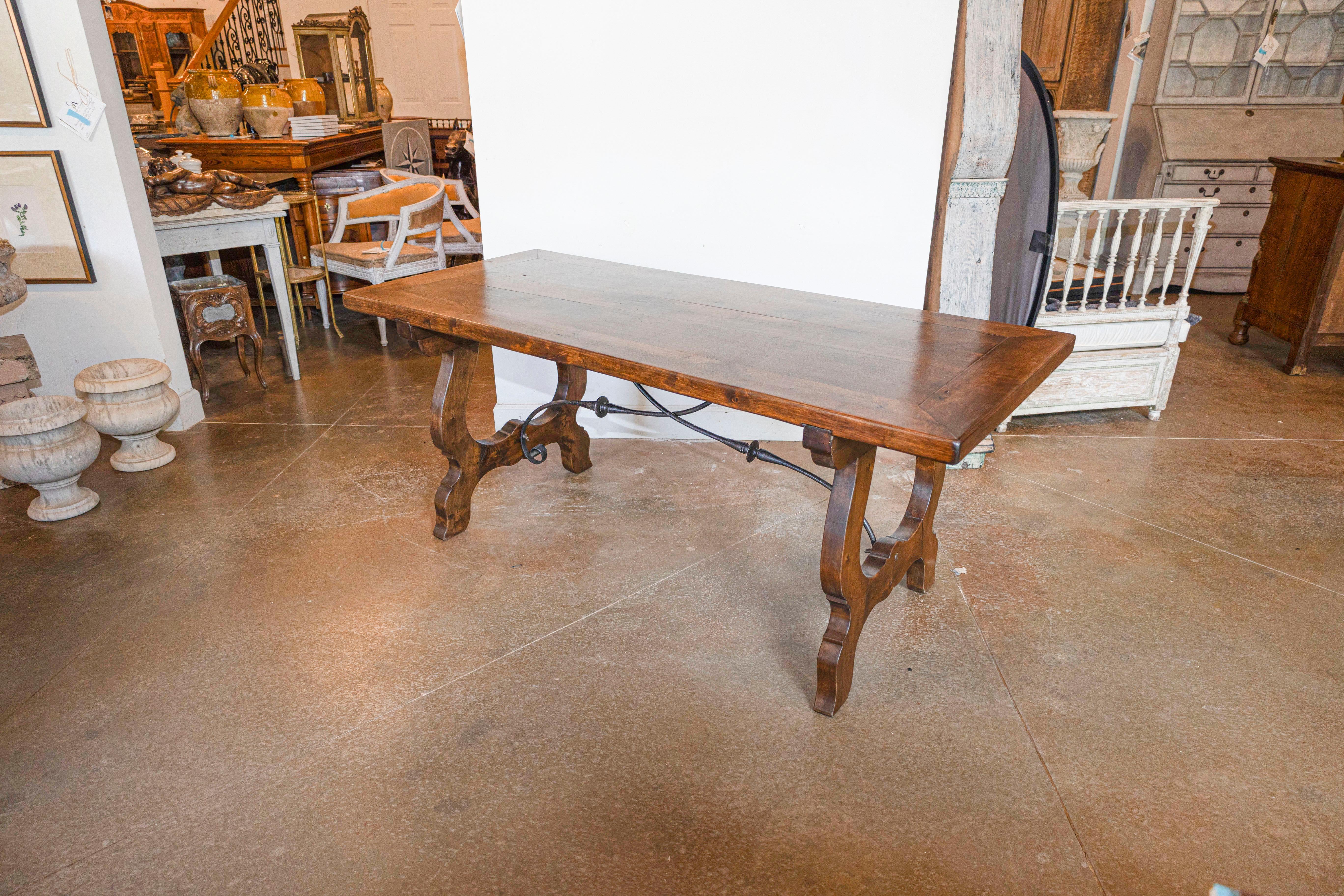 A Spanish Baroque style walnut fratino table with carved lyre shaped base and iron stretcher. Immerse yourself in the opulent world of Spanish Baroque style with this exquisite walnut fratino table, a piece that masterfully combines the drama and