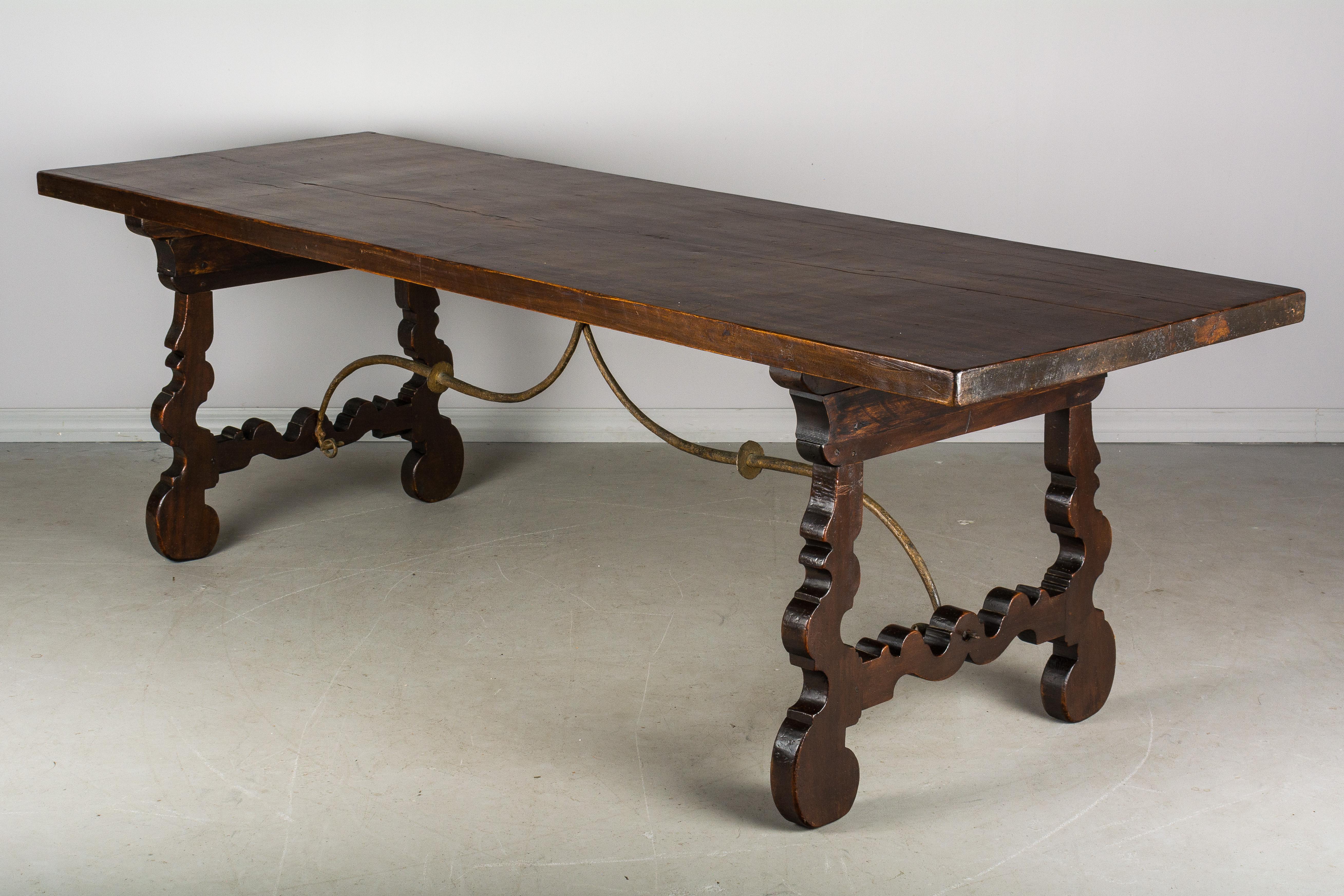 A Spanish Baroque style refectory table made of solid walnut with lyre shaped legs joined by wrought iron stretchers. The top is made from a single, 2