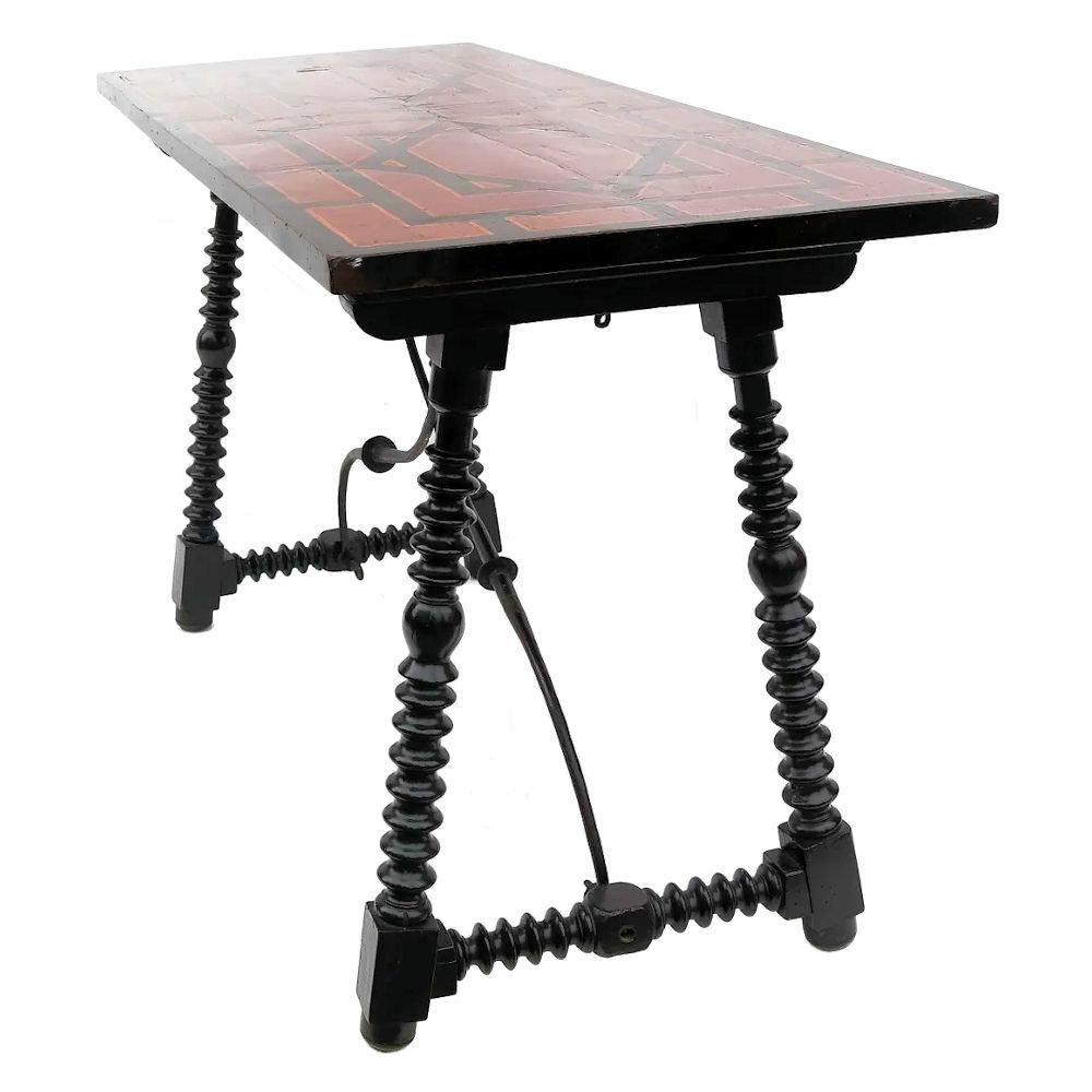Our Spanish Baroque trestle table dates from the 17th to 18th century and comes 27.5 by 49 by 19.75 inches. It features ebonized turned trestle legs with looping wrought iron supports, and rectangular varnished top with ebony and fruitwood veneers