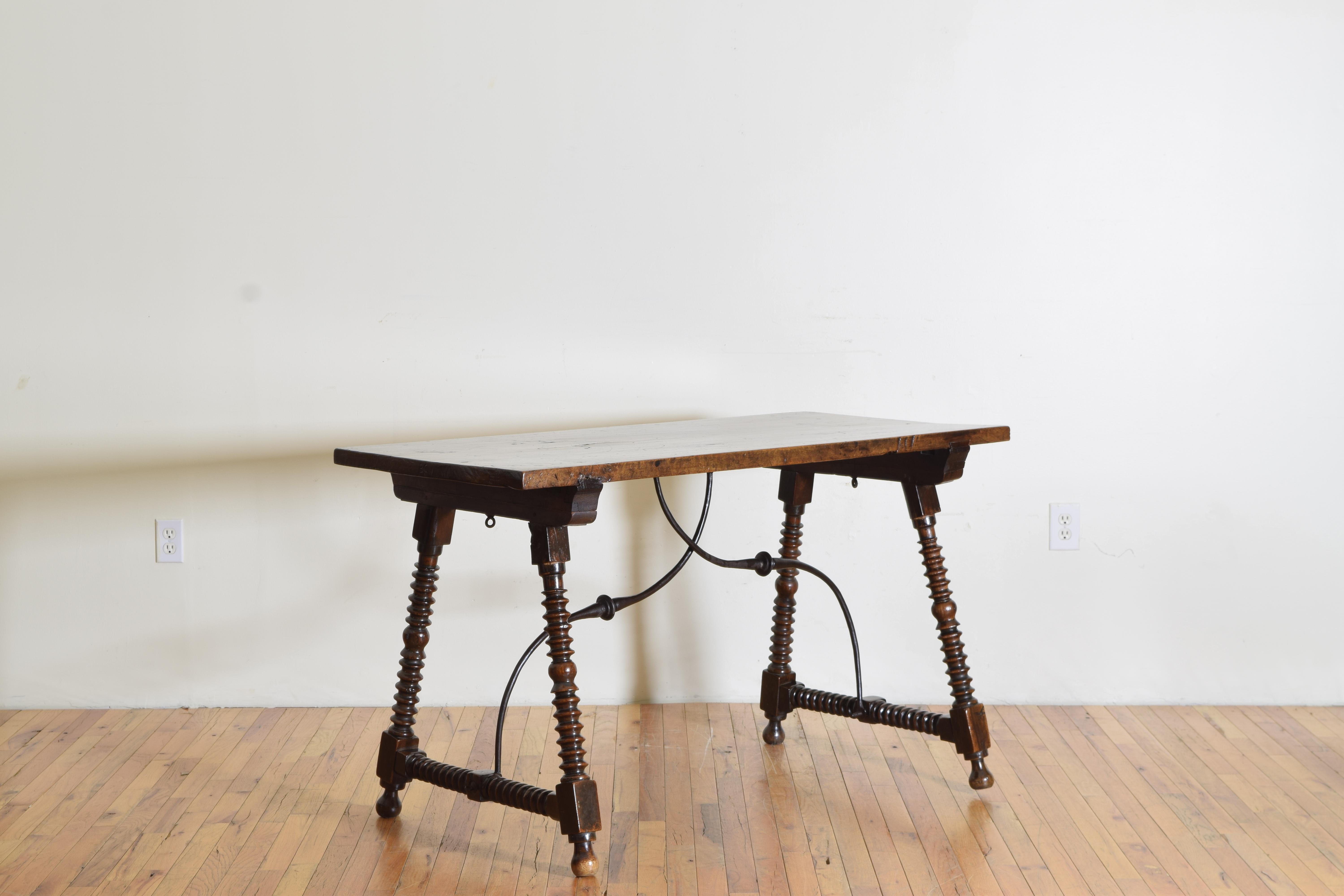 Having a solid rectangular one board top supported by turned trestle-form legs joined by original wrought iron stretchers, the table designed to fold or portability, raised on ball feet.
