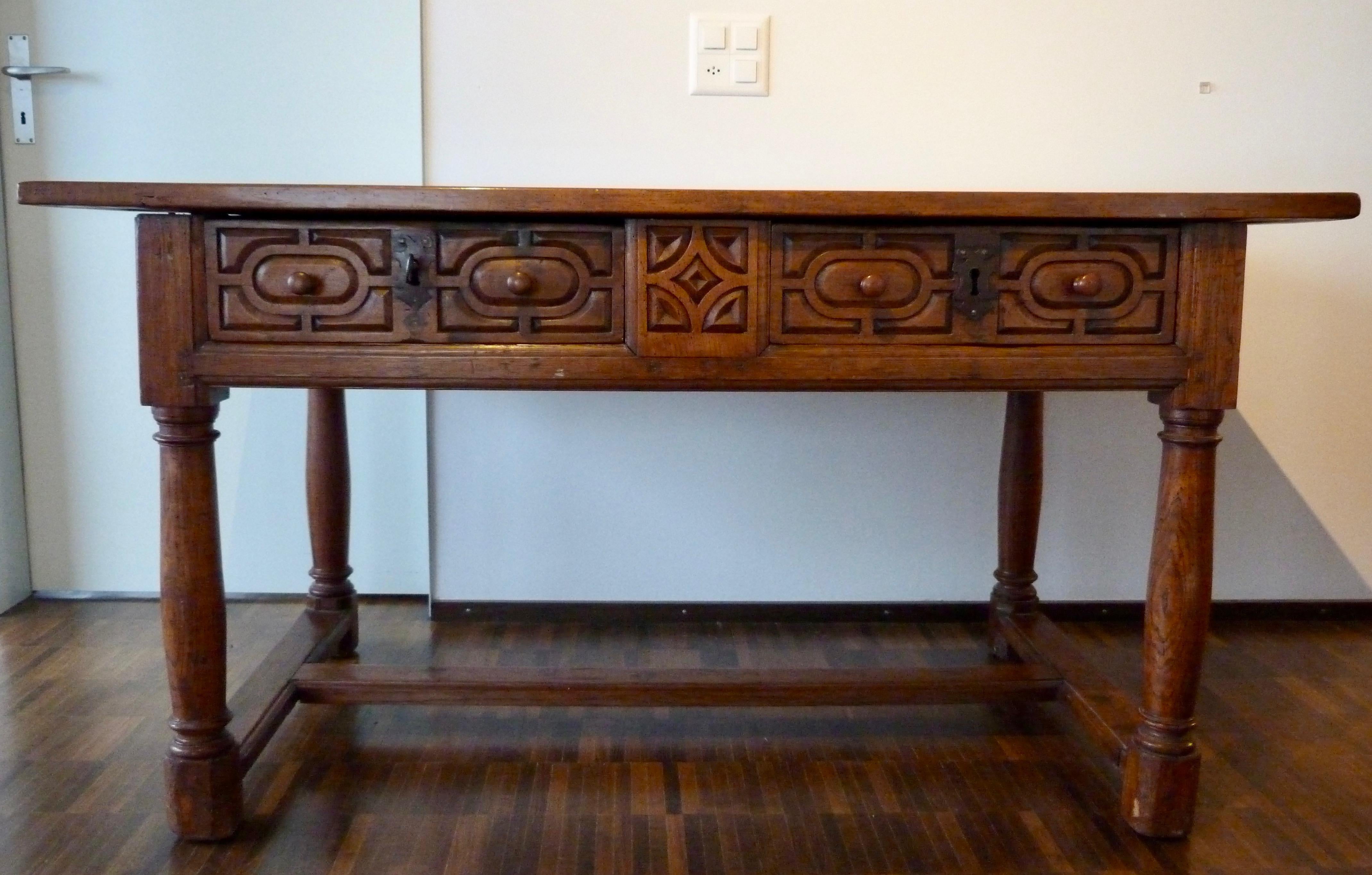 Spanish Baroque walnut desk table, late 17th century.

A rectangular single plank (1.25-inch thick) walnut top is sitting over 2 geometrical carved drawers with original handles and locks and all-around geometrical carved sides. The base is formed