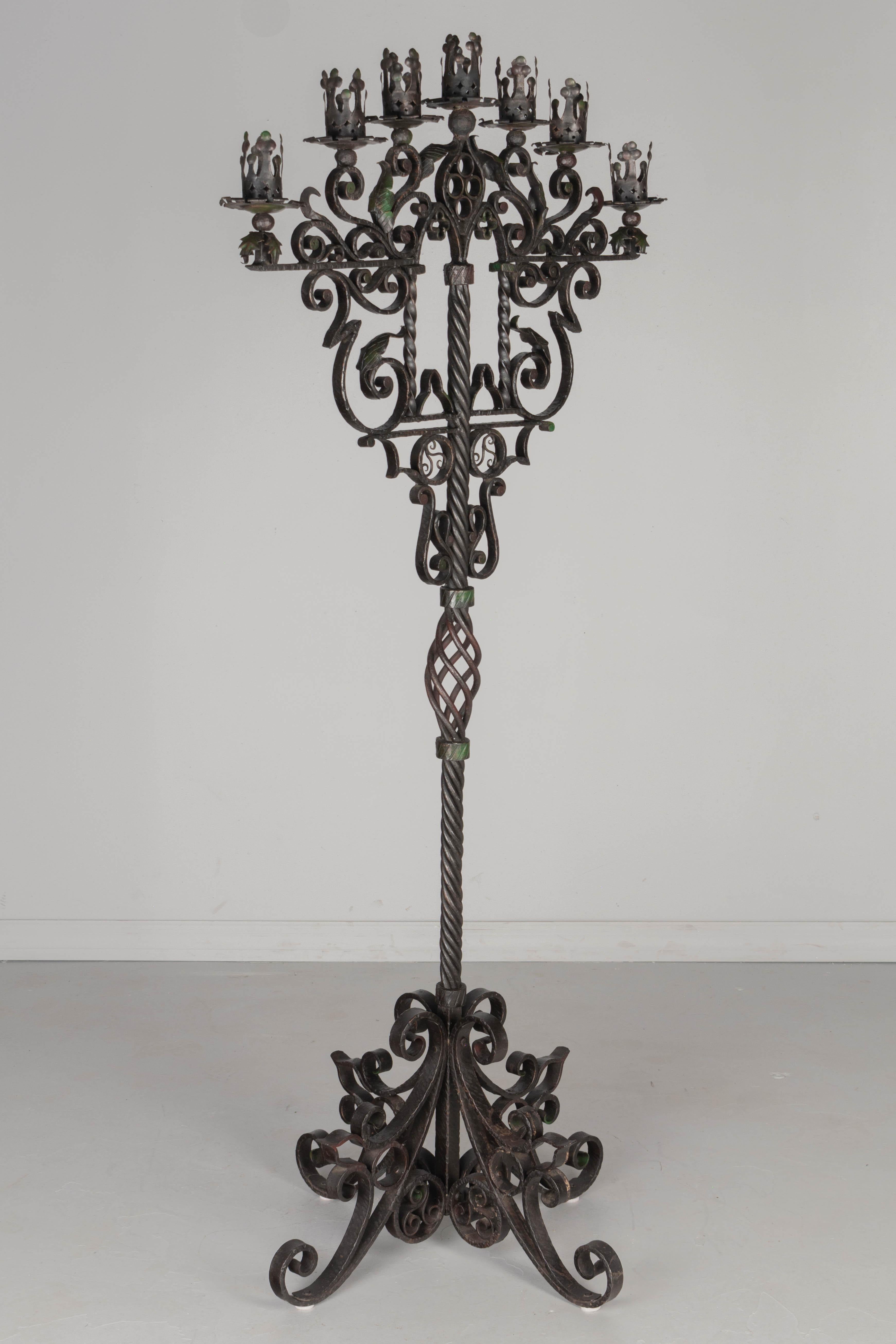 A large Spanish Baroque style wrought iron seven-light floor torchère, or candelabra with hand forged scrolling iron work and tôle acanthus leaves. Heavy base and thick center post with twisted center decoration. Black finish with some remnants of