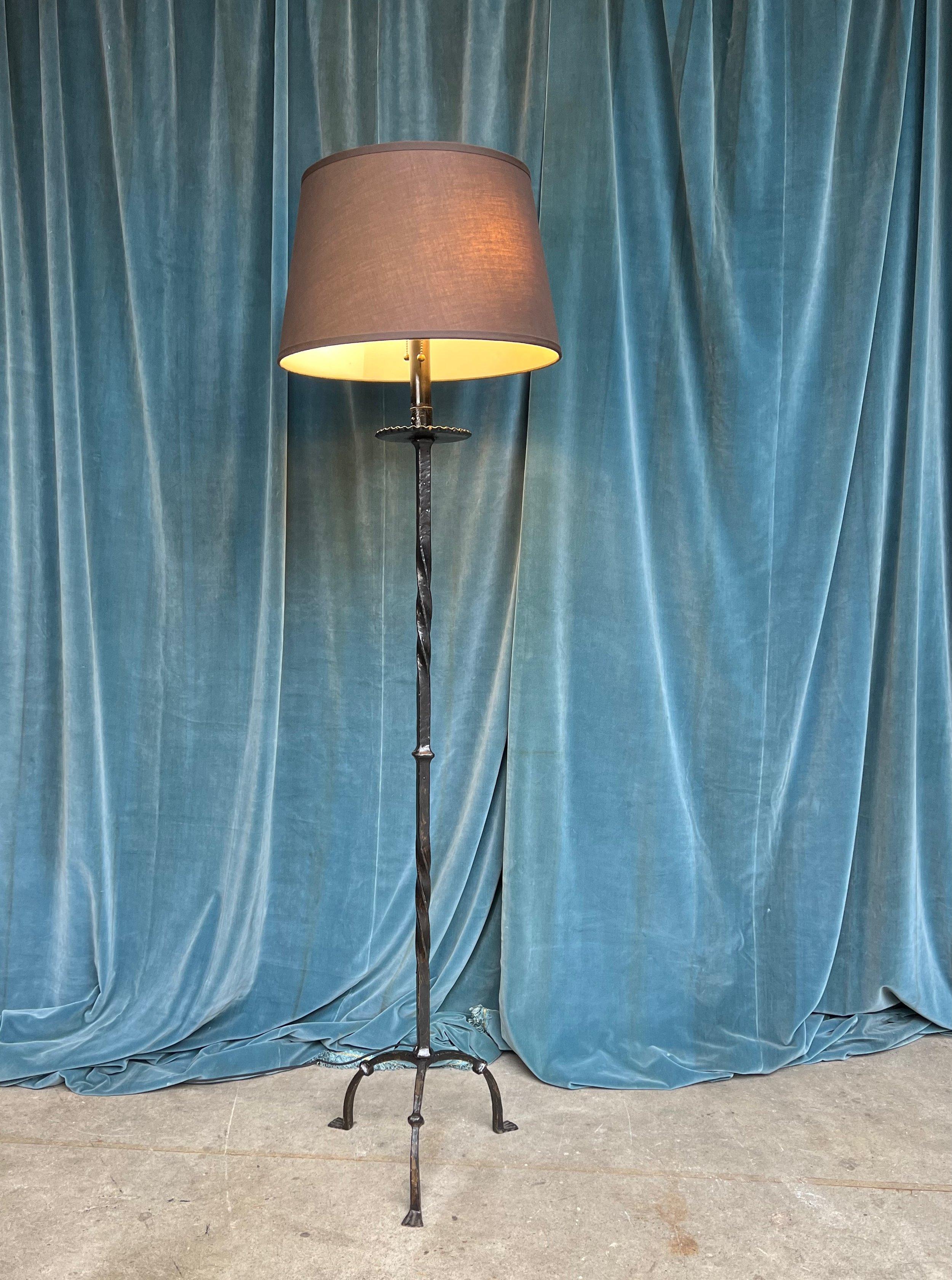 This floor lamp from the 1950s features a Spanish black painted iron construction, adding a touch of elegance and sophistication to any space. Its tripod base is complemented by decorative central elements, while the double twisted and spiraling