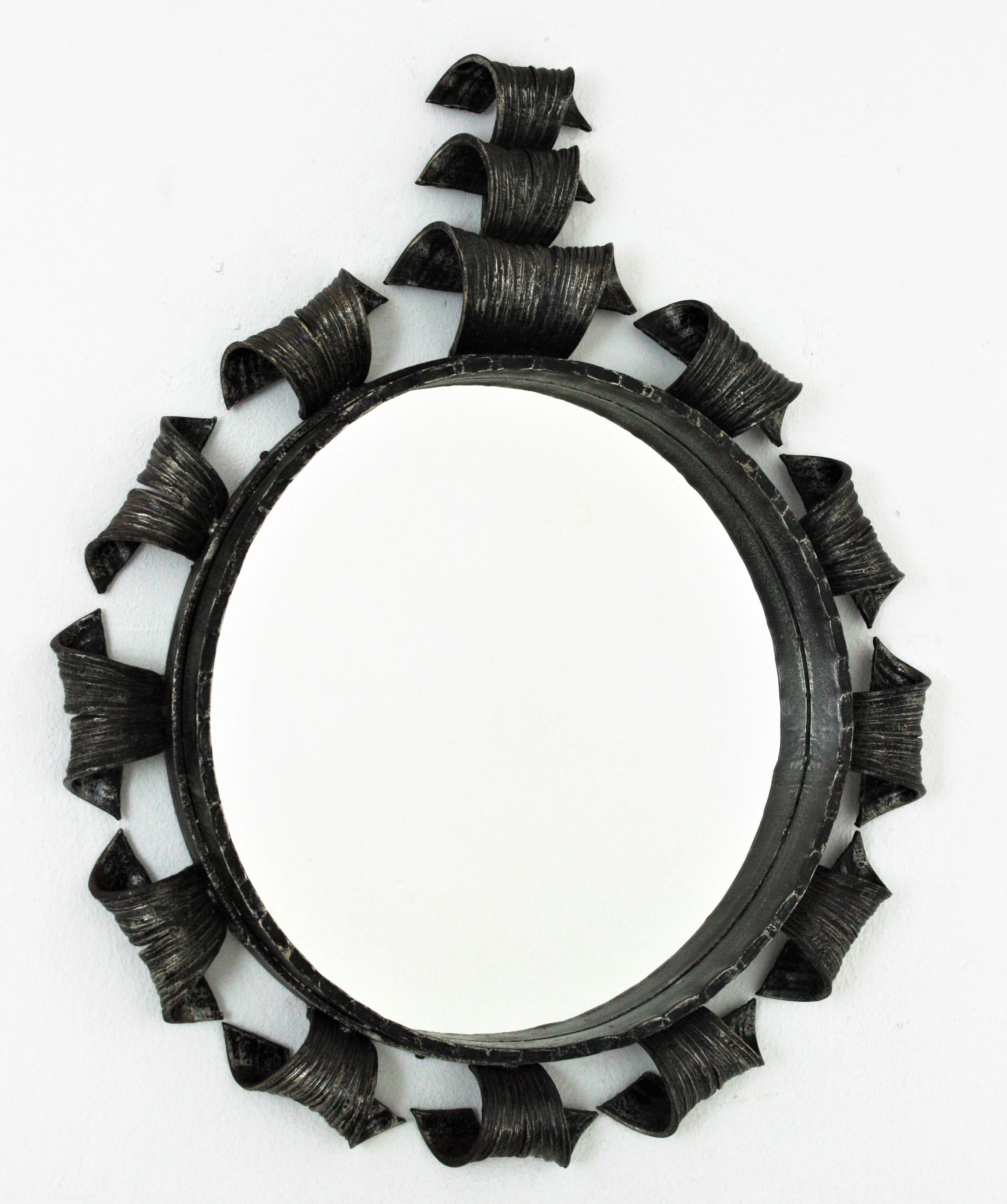Hand forged iron round mirror with scrolled details and crest, Spain, 1960s.
This eye-catching mirror is entirely made by hand. Brutalist idesign and a very heavy construction. The frame has thick scrollwork accents patinated in black with a crest