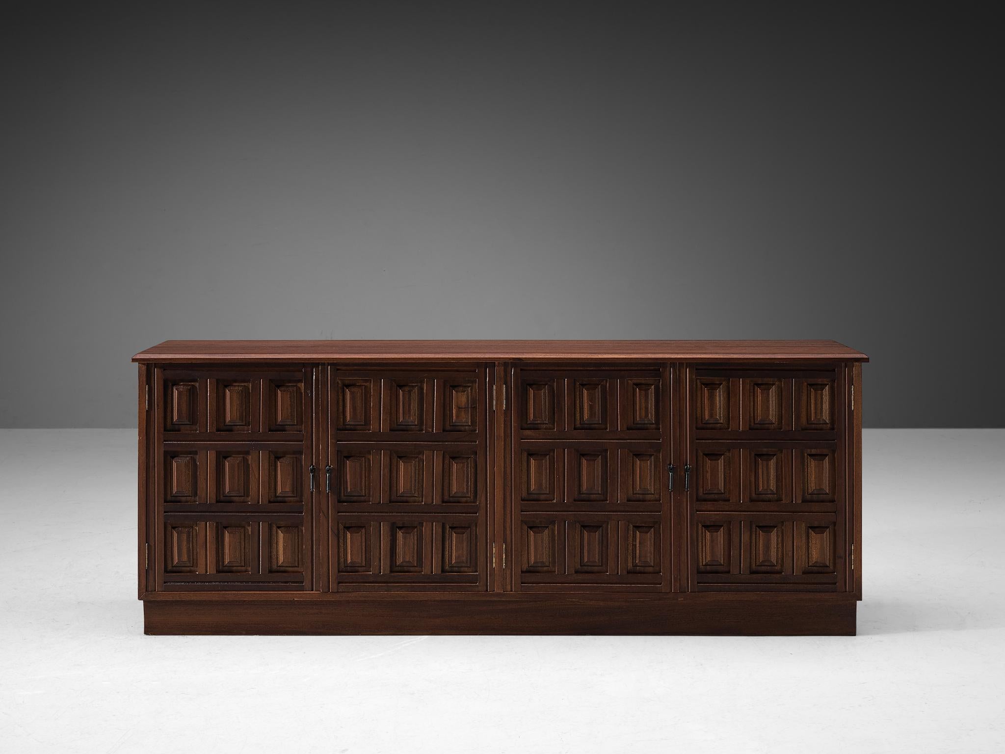 Sideboard, stained mahogany, metal, Spain, 1970s.

This very evocative sideboard features a clear rhythm and flow established by means of a well thought through lay out that is utterly well-balanced. The carved geometric shapes on the door panels