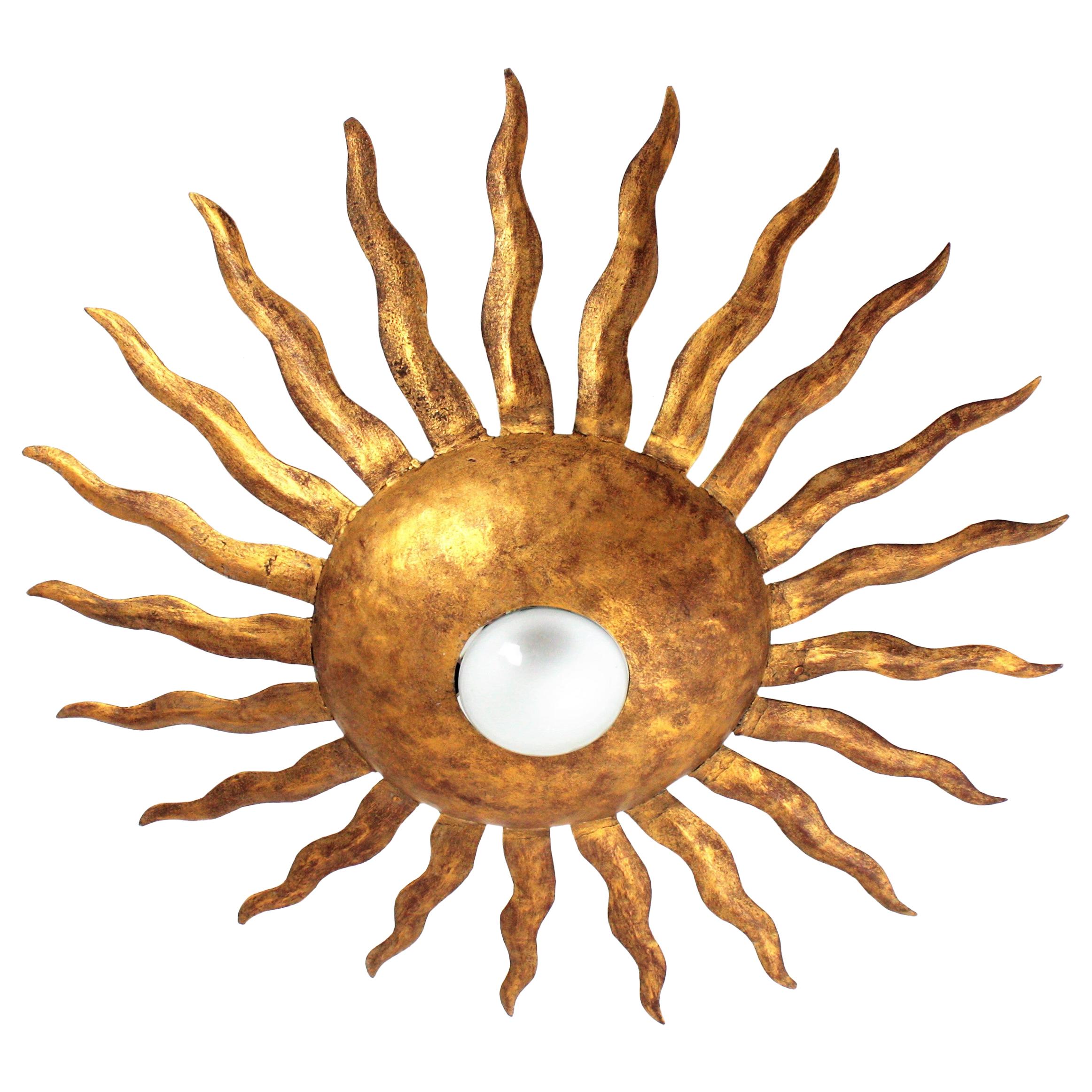 A beautiful sunburst ceiling light fixture or flushmount with gold leaf finish made in wrought iron, Spain, 1950-1960.
It has beautiful details of thick rays surrounding the central sphere with an exposed bulb.
It can be placed as a wall sconce or