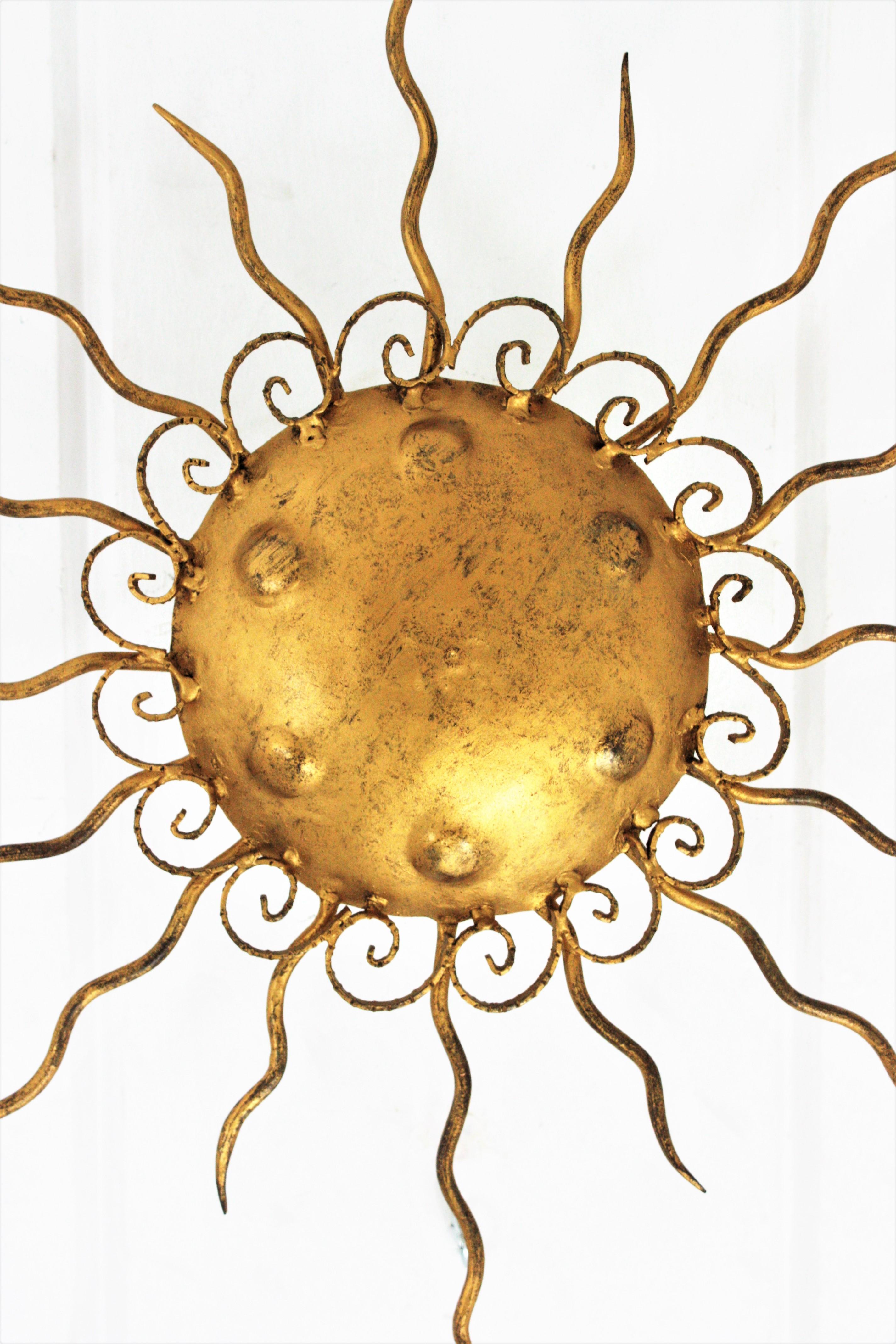 Gold leaf gilt iron sunburst flush mount or wall sconce from the Brutalist period. Spain, 1950s.
Richly decorated with scrolls surrounding the central shade and engraved circles. 
Beautiful to place as ceiling light fixture but also as wall