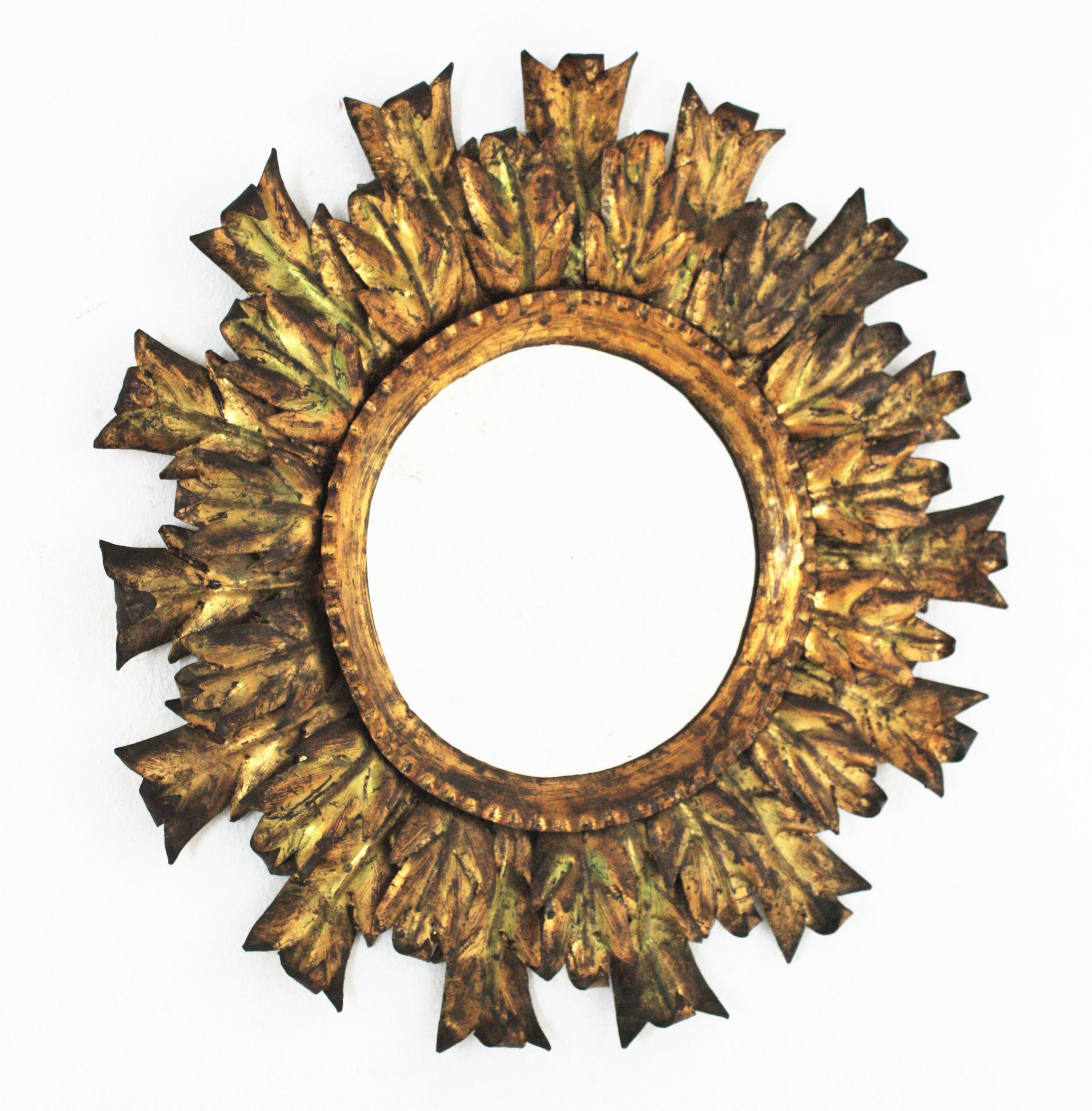 Gilt metal leafed sunburst mirror, Spain, 1940s-1950s.
This handcrafted Brutalist wall mirror features two layers of alternating leaves in different sizes surrounding a central round glass. It has a terrific aged patina with gold leaf finish and