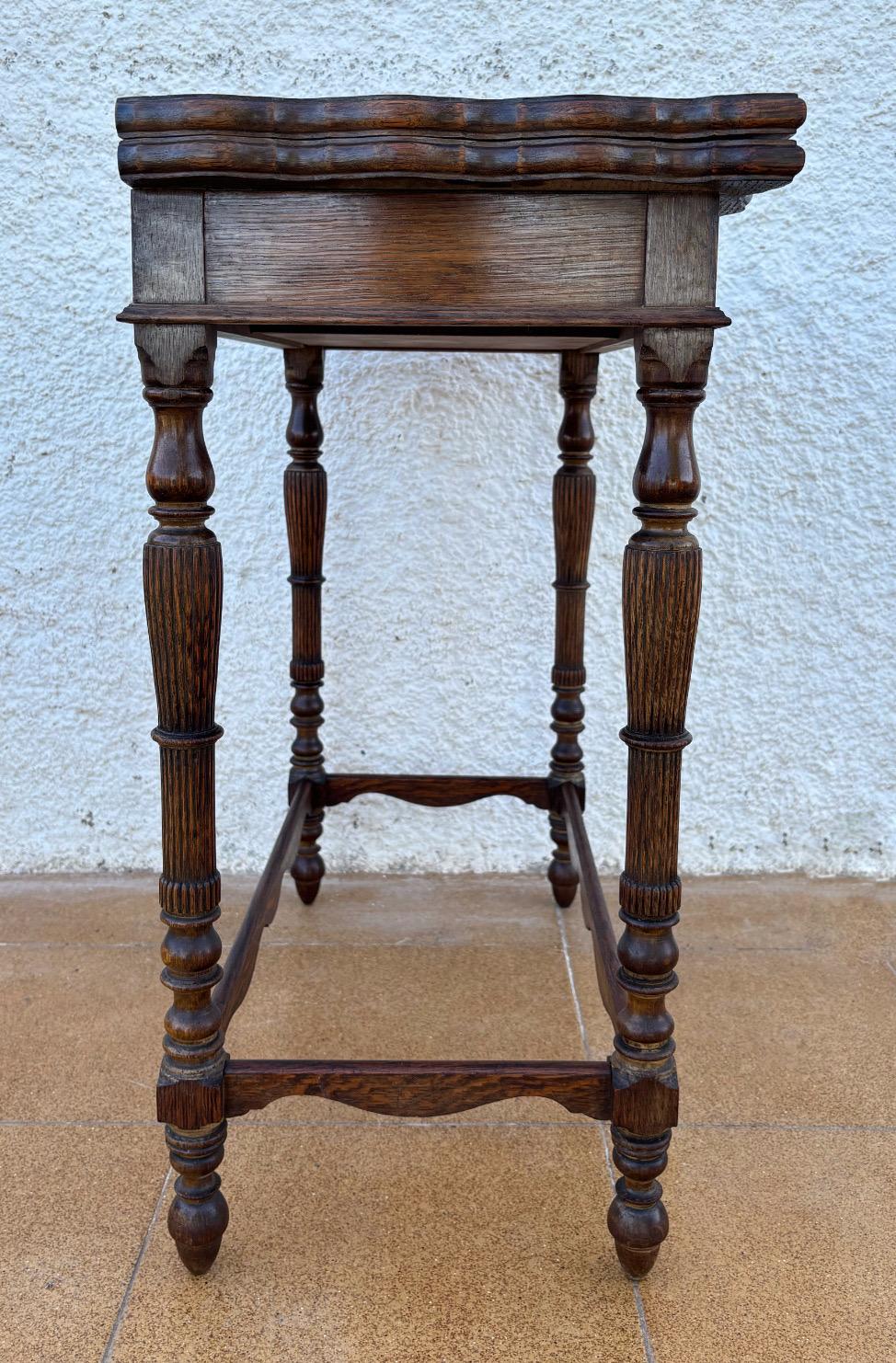 Cette table de jeu espagnole raffinée des années 1920 présente un magnifique cadre en chêne aux bords sculptés et d'élégants pieds tournés. Le dessus en feutre vert d'origine ajoute un caractère d'époque distinctif, offrant un contraste vibrant avec