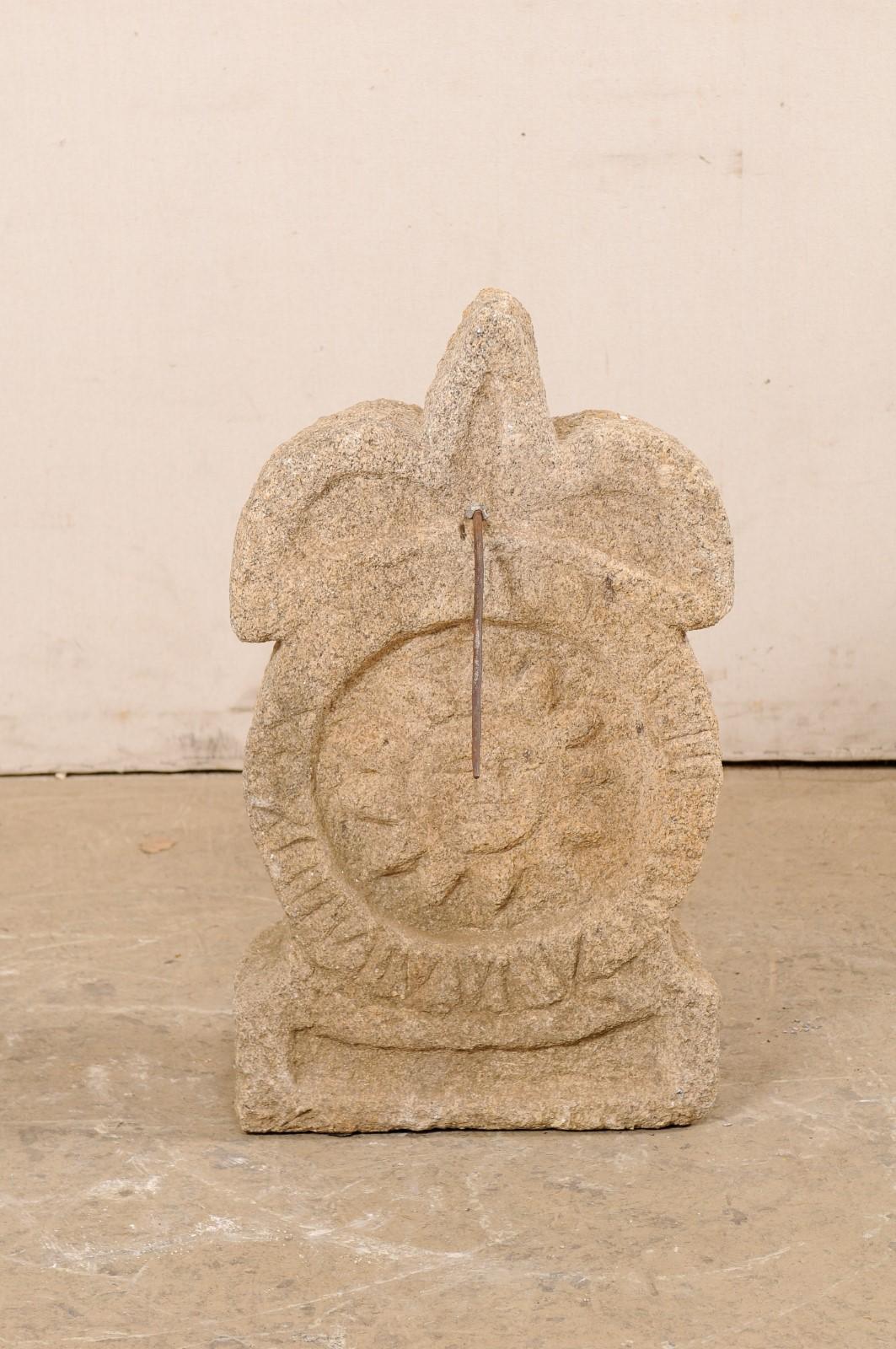 A Spanish carved-stone sundial in fleur de lys motif. This vintage sundial from Spain has been hand-carved from a single piece of stone and features a fleur de lys crest top, over a rounded body with a sun-carved center within roman numerals set