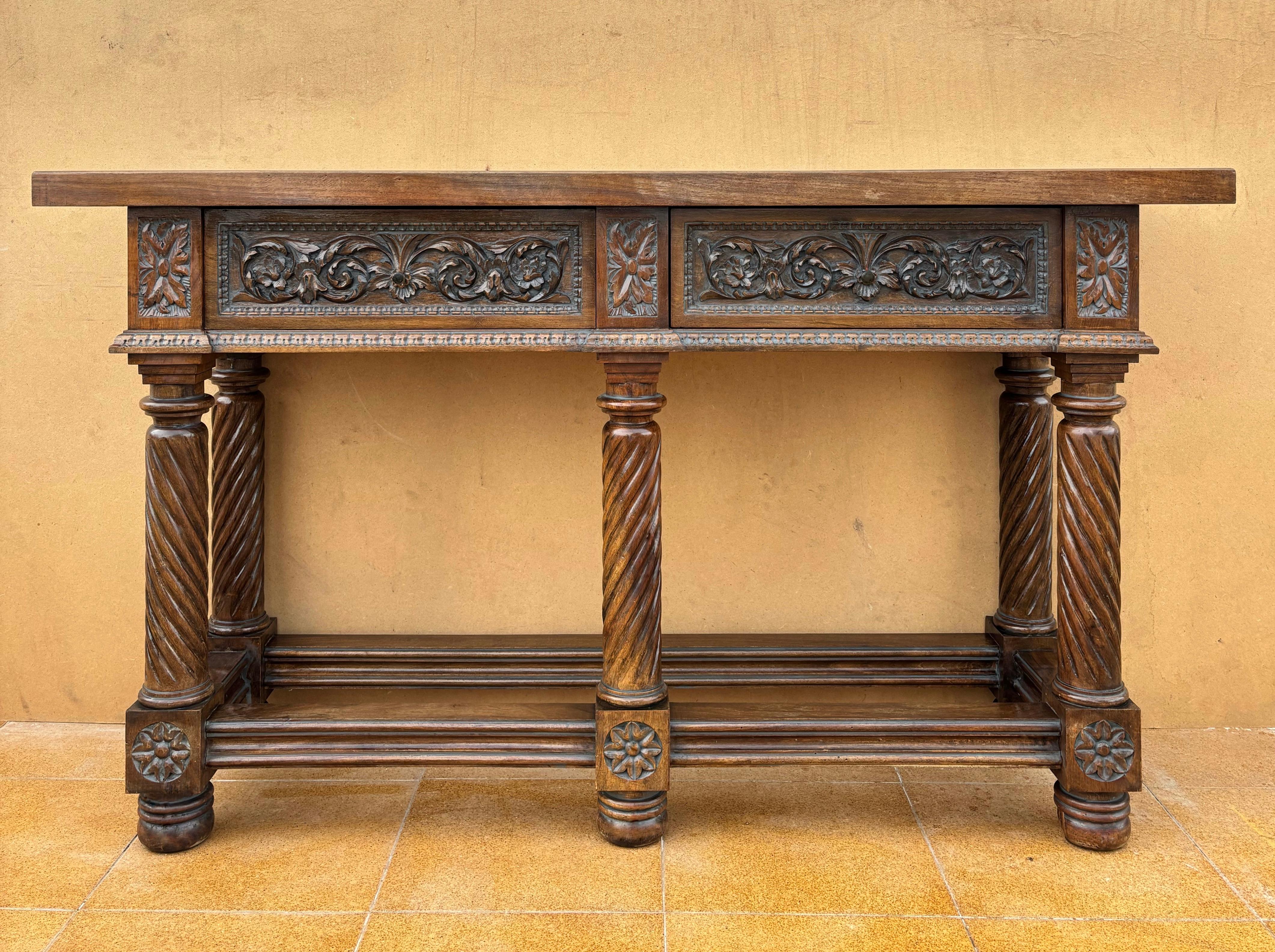 Questa elegante consolle spagnola, risalente al 1890 circa, è realizzata in noce massiccio e riccamente decorata con motivi rinascimentali intagliati a mano. Il frontale presenta due cassetti ornati da profondi intagli floreali e fogliacei in