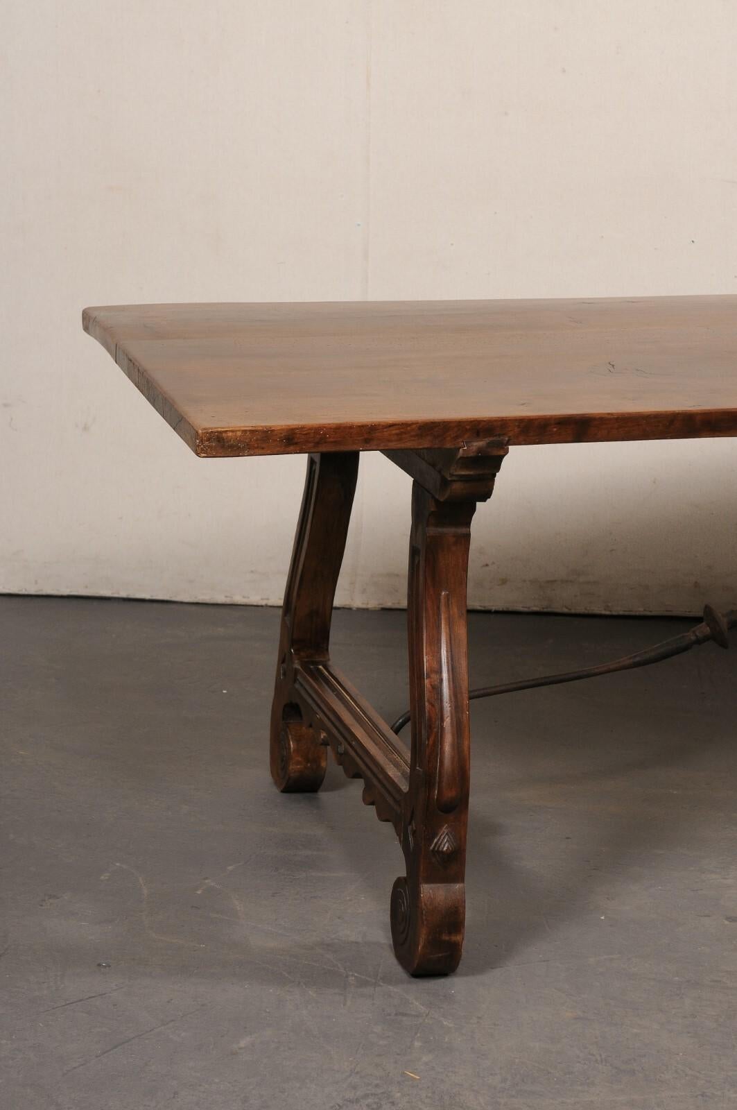 A gorgeous Spanish carved-walnut trestle table with iron stretcher from the mid 20th century. This vintage table from Spain features a rectangular shaped top, just over 8 feet in length, raised upon a pair of fluidly-carved trestle legs adorn with