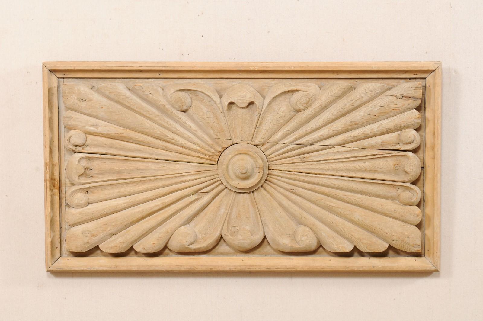 A Spanish carved wood plaque from the early 20th century. This antique natural wood wall plaque from Spain has a rectangular-shape, and features a carved stacked circle at centre, with rays extending in outward fashion, curling at their tips, all