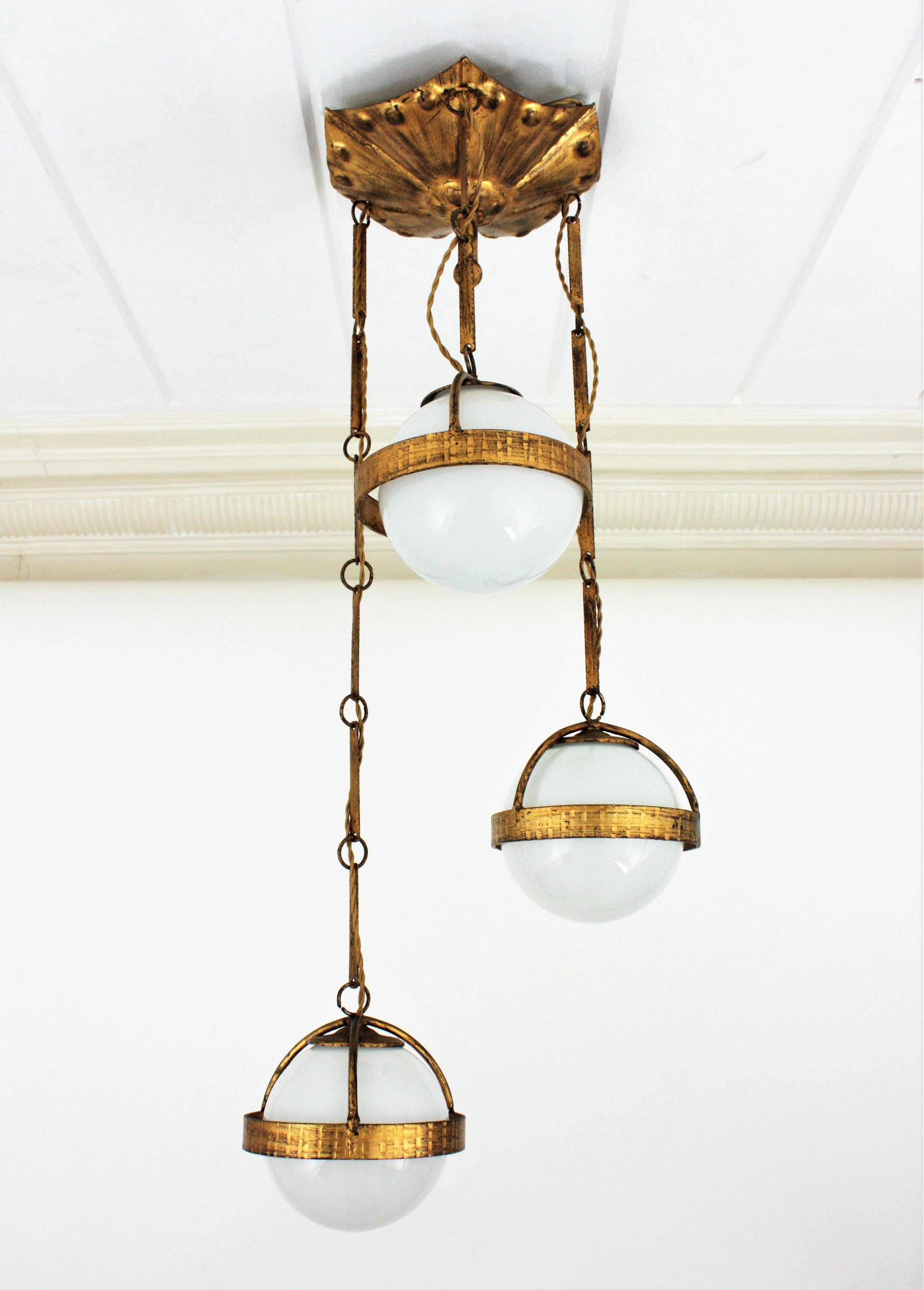 Amazing hand forged gilt iron cascading pendant with three opaline glass globes, Spain, 1940s.
This eye-catching pendant features a massive gilt iron canopy holding three glass globe shades surrounded by a ring structure hanging from chains
