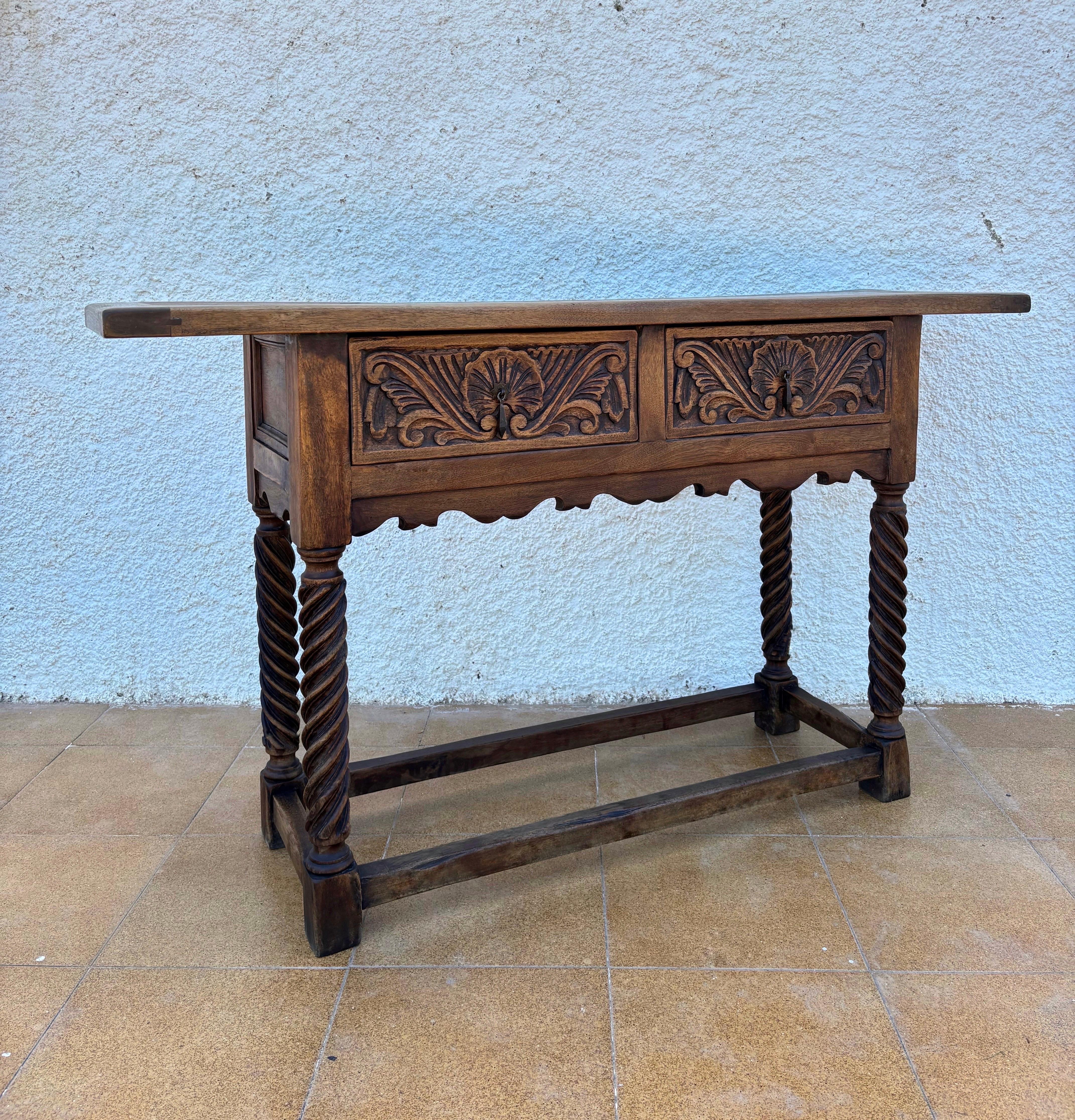Beautiful Spanish console table handcrafted in solid oak, dating from the early 20th century and inspired by traditional Baroque / Castilian furniture design. This charming piece features two front drawers richly decorated with hand-carved foliate