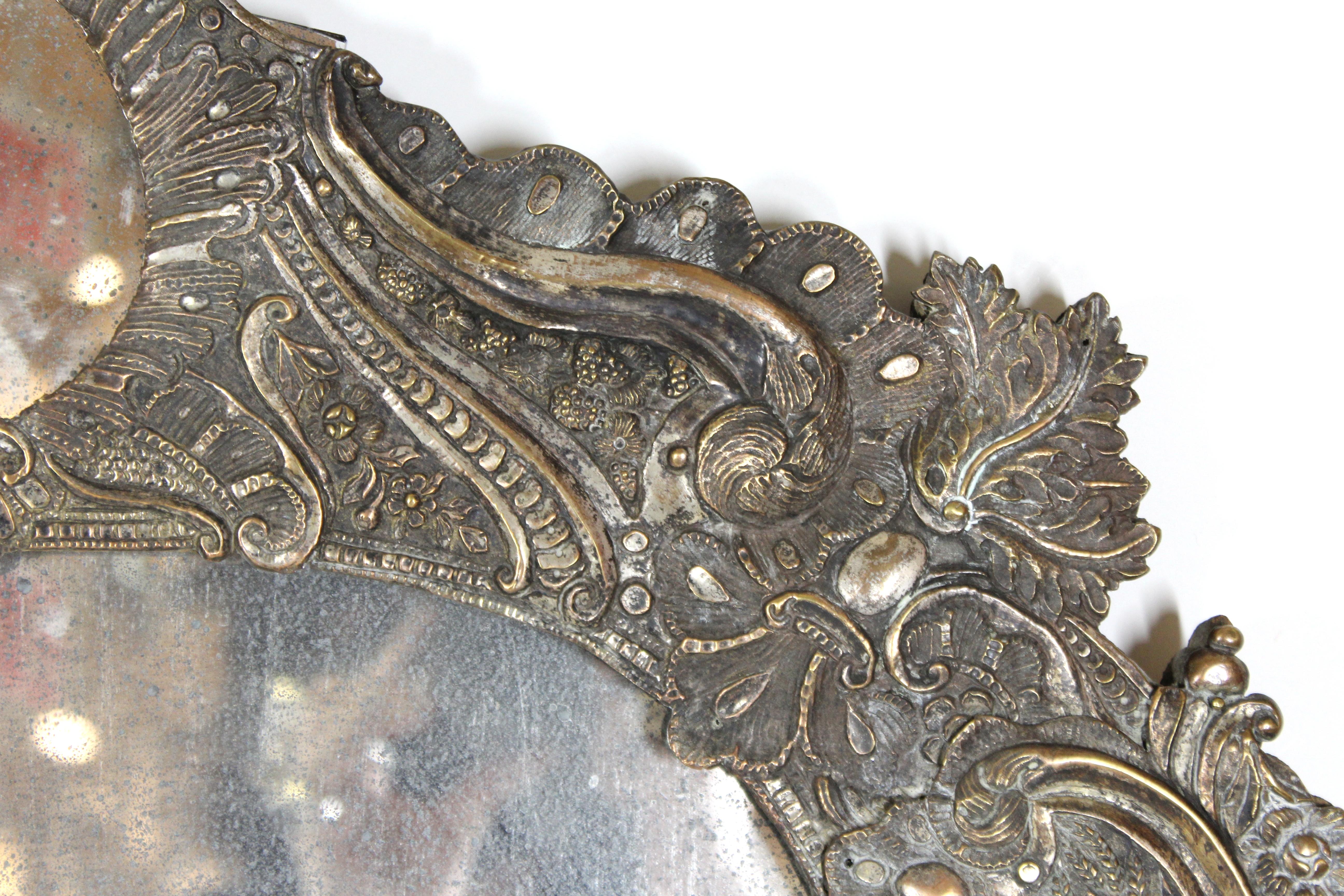 Spanish colonial Baroque elaborate mirror frame in repoussé silver on wood frame. The piece has a vast amount of baroque volutes and scrolls ornamentation, with depiction of wheat, berries and flowers around the border. A smaller ovoid shape mirror