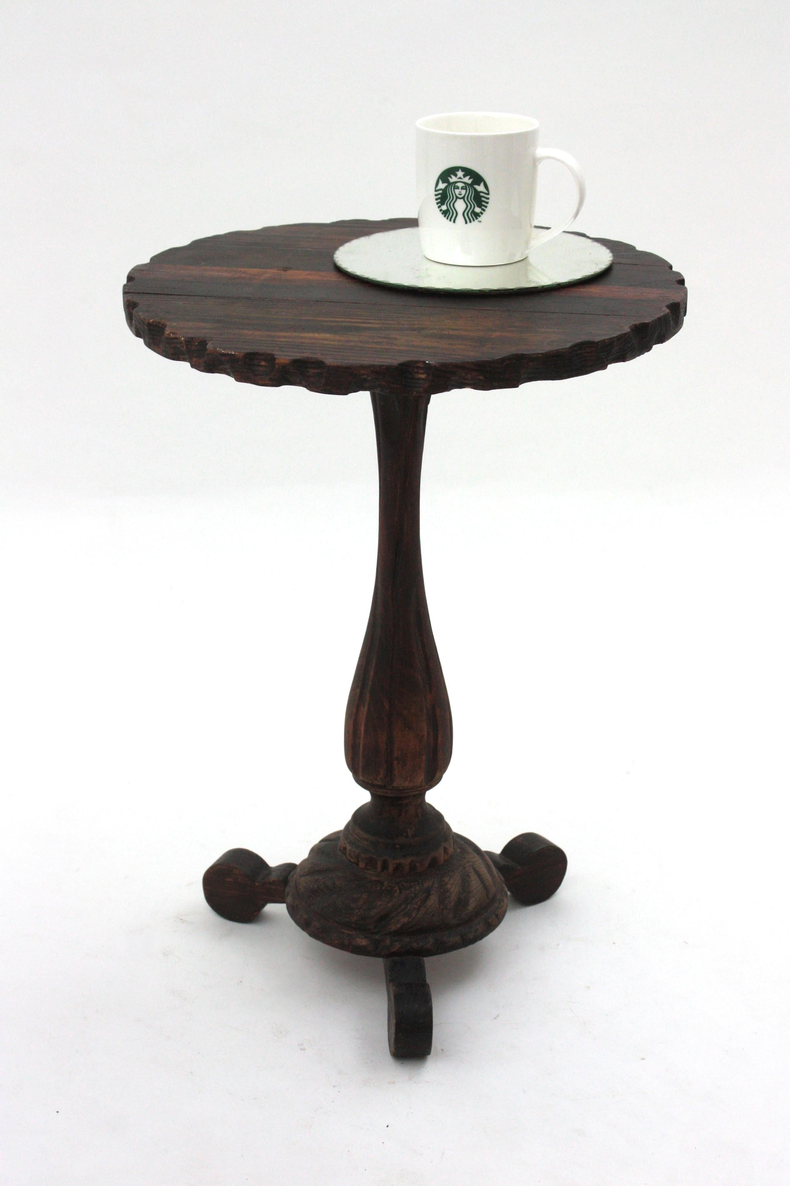 Mesa gueridón o mesa ocasional de madera de pino tallada a mano sobre base de trípode. España, década de 1940.
El tablero de forma redonda con borde festoneado se apoya en una base de tres patas con detalles retorcidos. El tallo también está
