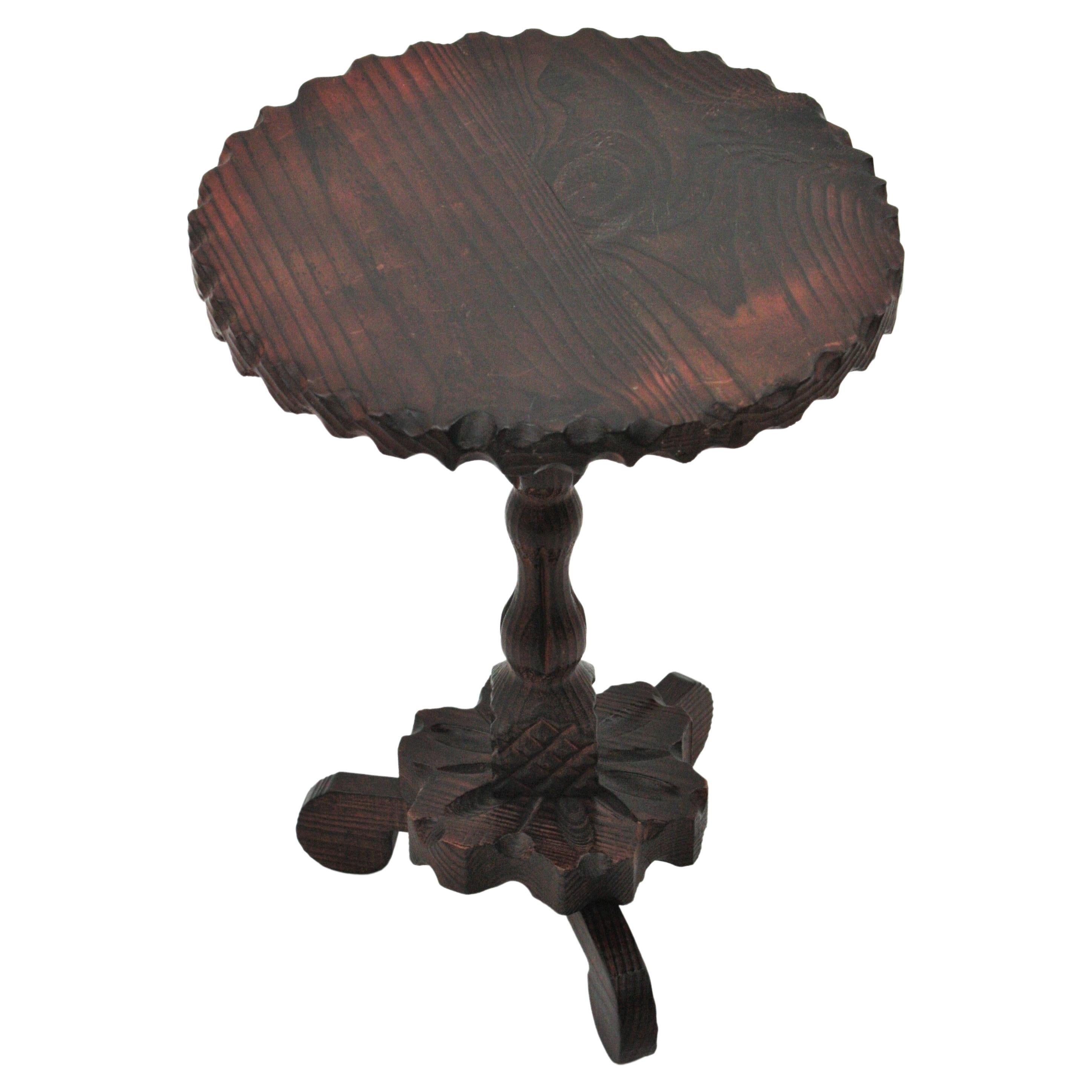 Handgeschnitzter Gueridon-Tisch oder Beistelltisch aus Kiefernholz auf einem Dreibeinfuß. Spanien, 1940er Jahre.
Die runde Tischplatte ist am Rand mit einem Wellenschliff versehen. Er steht auf einem gedrechselten Holzstiel auf einem blumenförmig