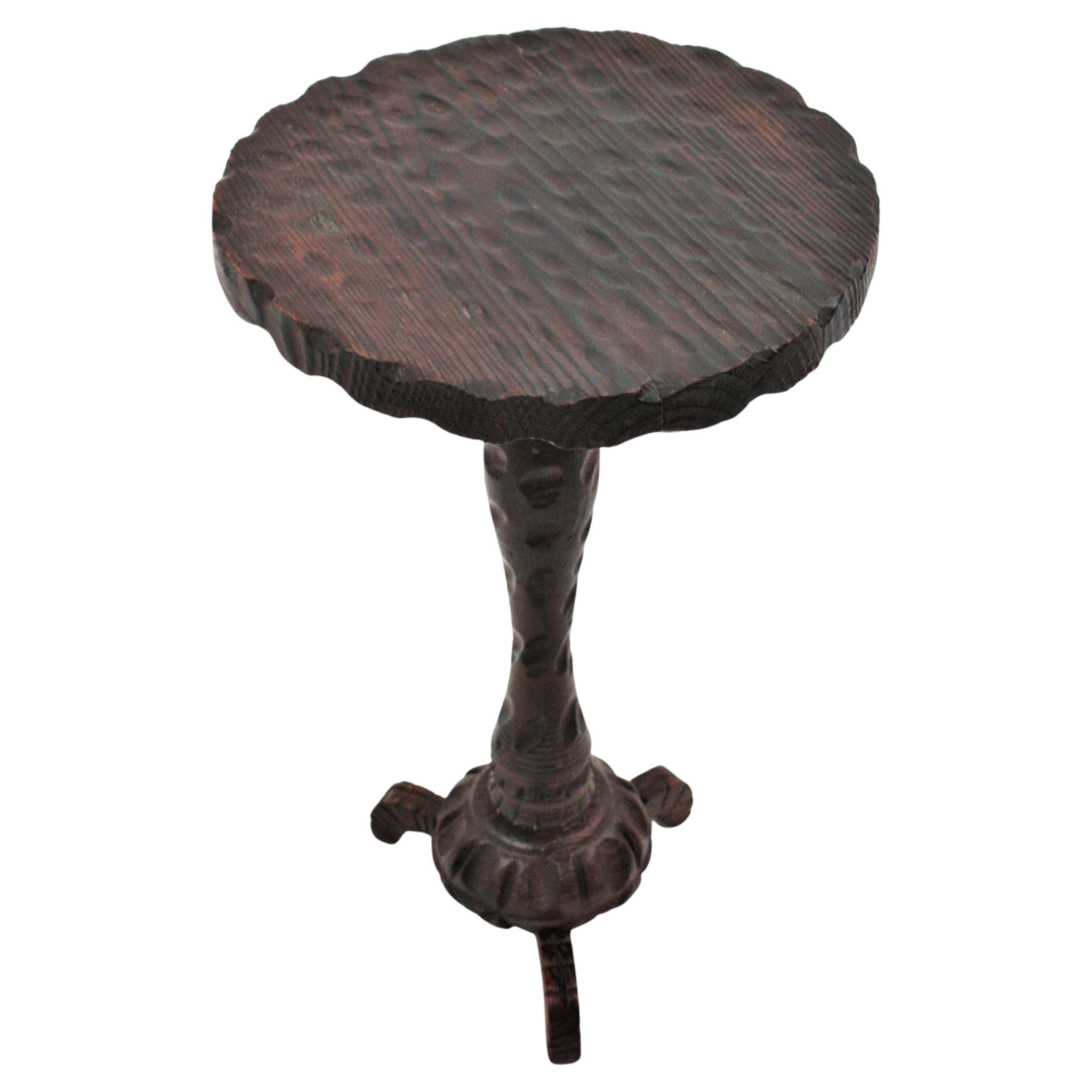 Handgeschnitzter Gueridon-Tisch oder Beistelltisch aus Kiefernholz auf einem Dreibeinfuß. Spanien, 1940er Jahre.
Die Tischplatte in runder Form hat eine Wellenform am Rand und schöne Schnitzereien. Er steht auf einem Holzstiel mit geschwungenen