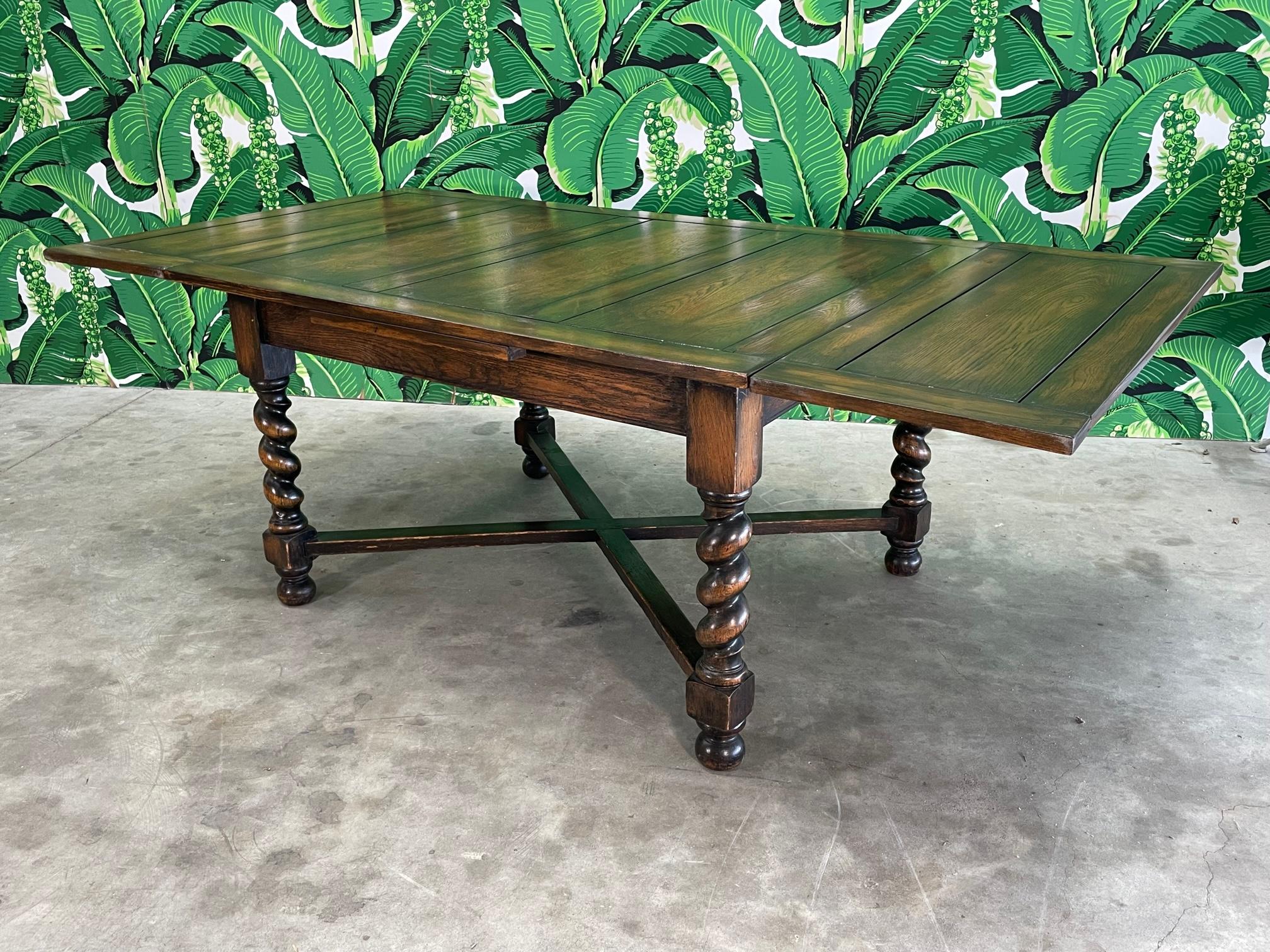 Carved wood dining table in Spanish colonial style. Heavy and substantial. Good vintage condition with imperfections consistent with age, see photos for condition details. Holds 2 retractable leaves, each 16