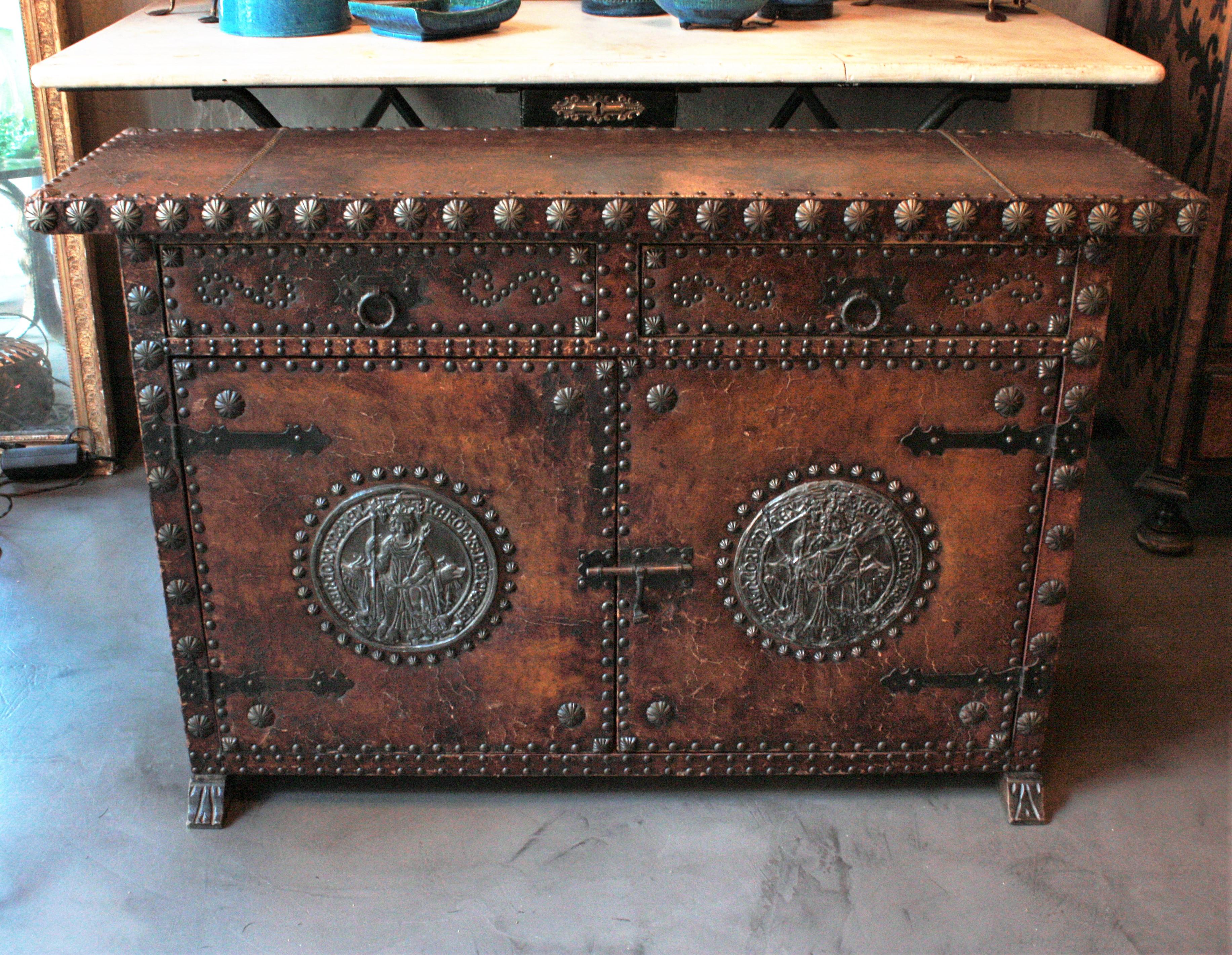 Terrific traditional leather and wood cabinet or sideboard with studwork and decorative panels, Spain, 1940s.
This handsome cabinet has two drawers over two doors. It is upholstered in brown leather which is decorated with large silvered studs and