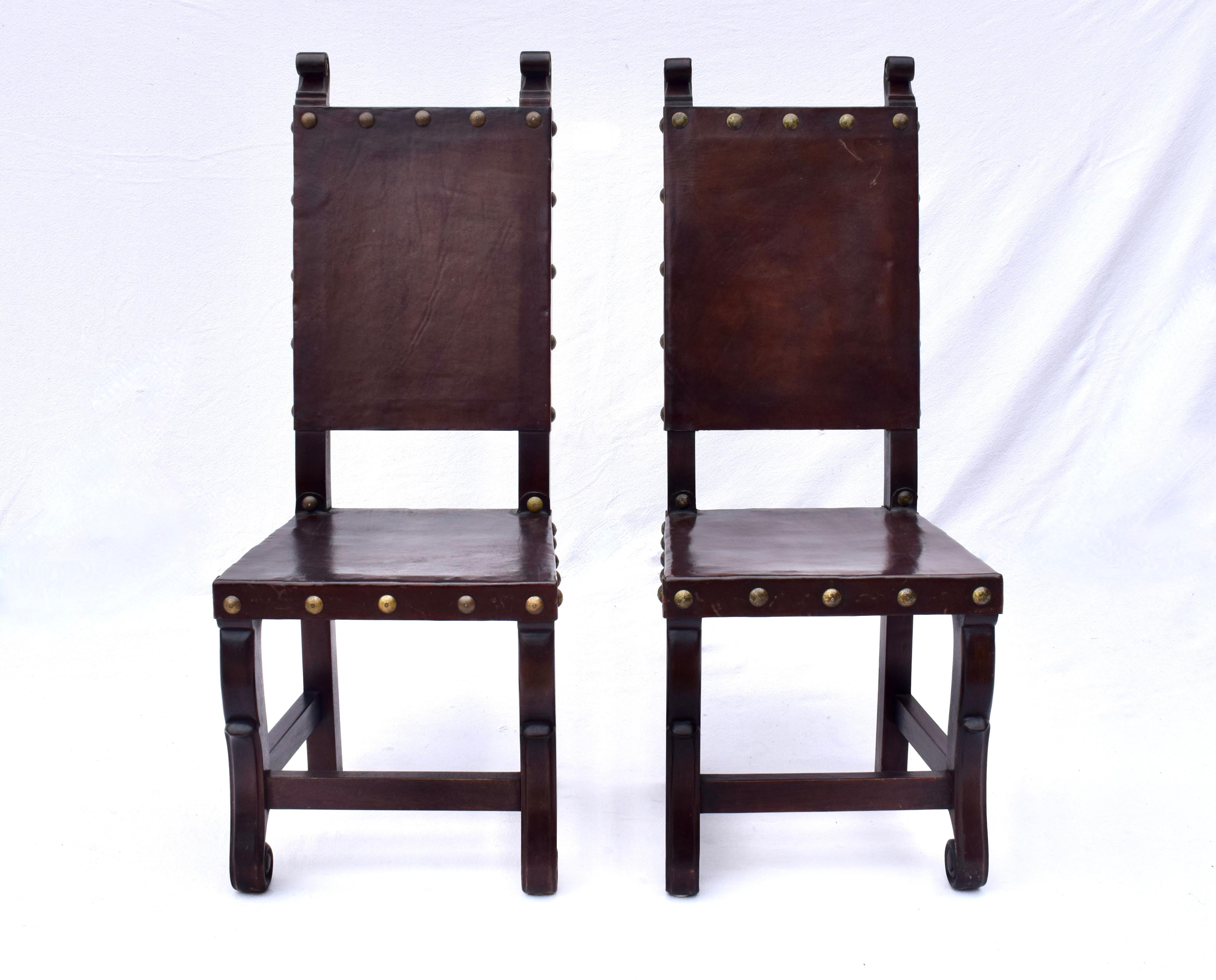 Fabulous  pair of carved wood dining chairs with thick leather seats & backs embellished with brass nail heads in the Spanish Colonial style. Gorgeous rock solid condition ready for use.
