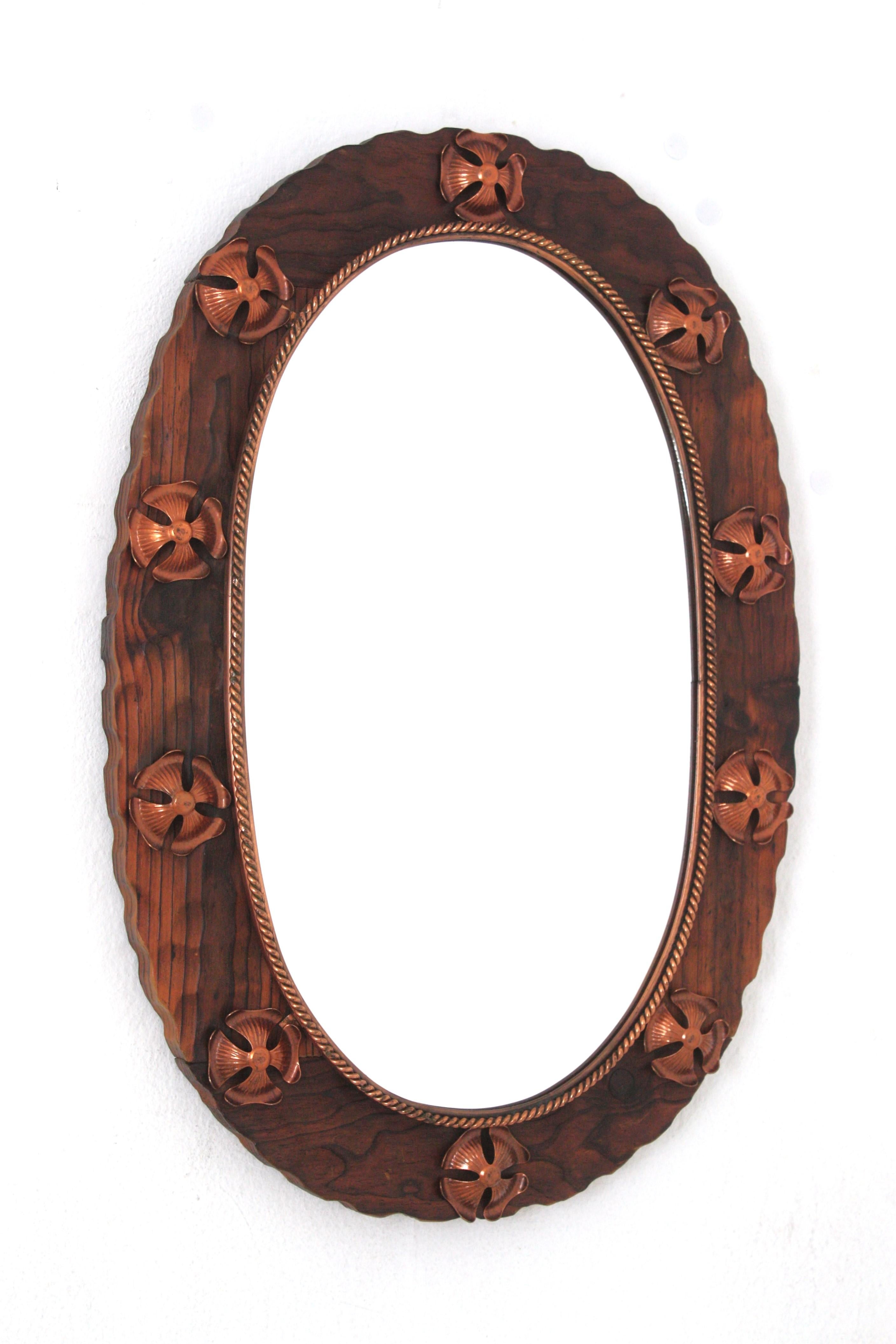 Hand carved pine wood oval wall mirror with copper flower details, Spain, 1940s.
This wall mirror features a wooden scalloped frame surrounding a central oval glass with a twisted copper pattern. Turned wood details and 10 copper flowers are