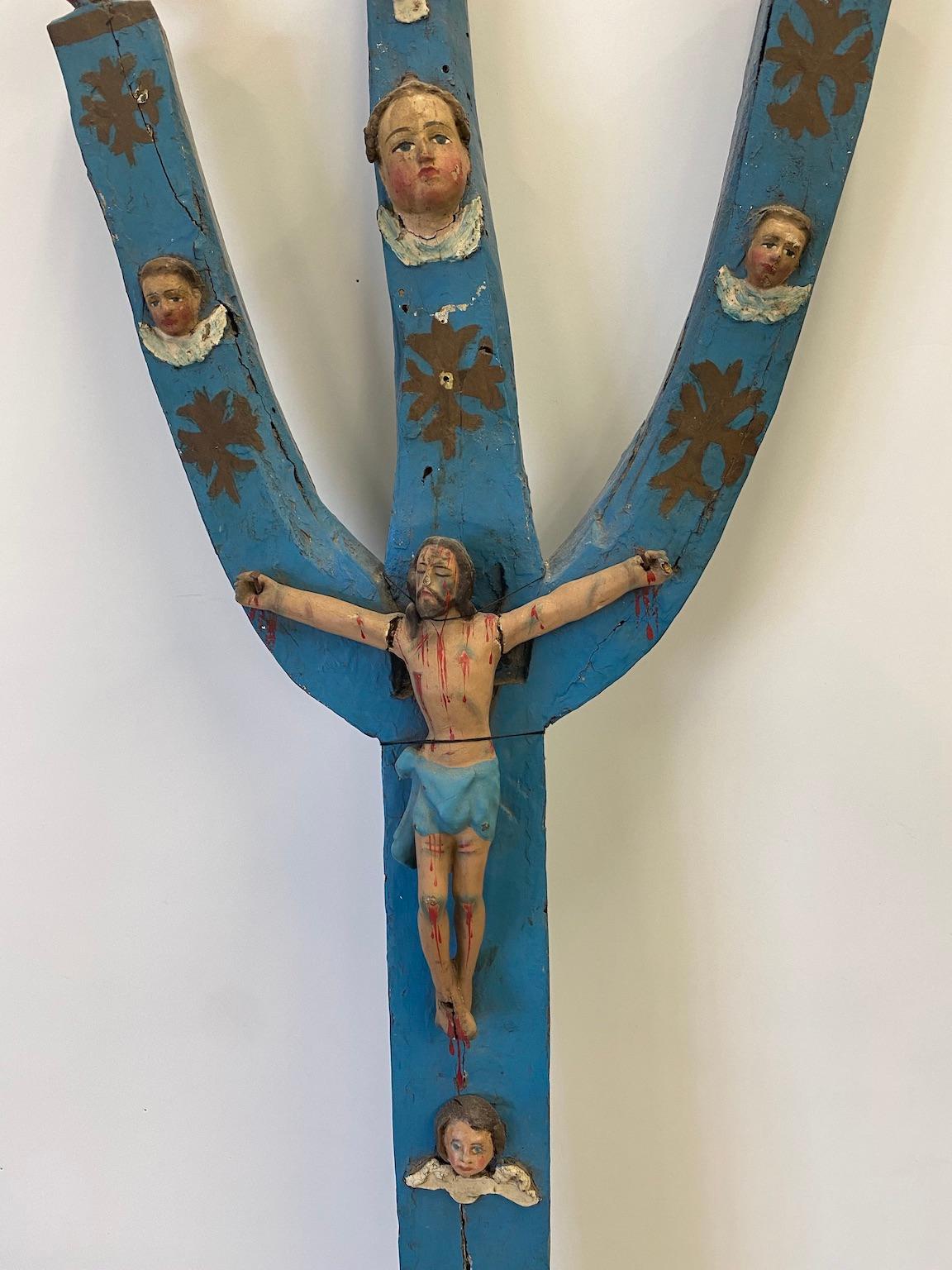This carved wooden crucifix of Christ on a stylized tree form, is Guatemalan or Mexican, likely created in the late 1800s by a naive artist of the period, 19th century. It has been painted, and perhaps repainted, through the years. This devotional