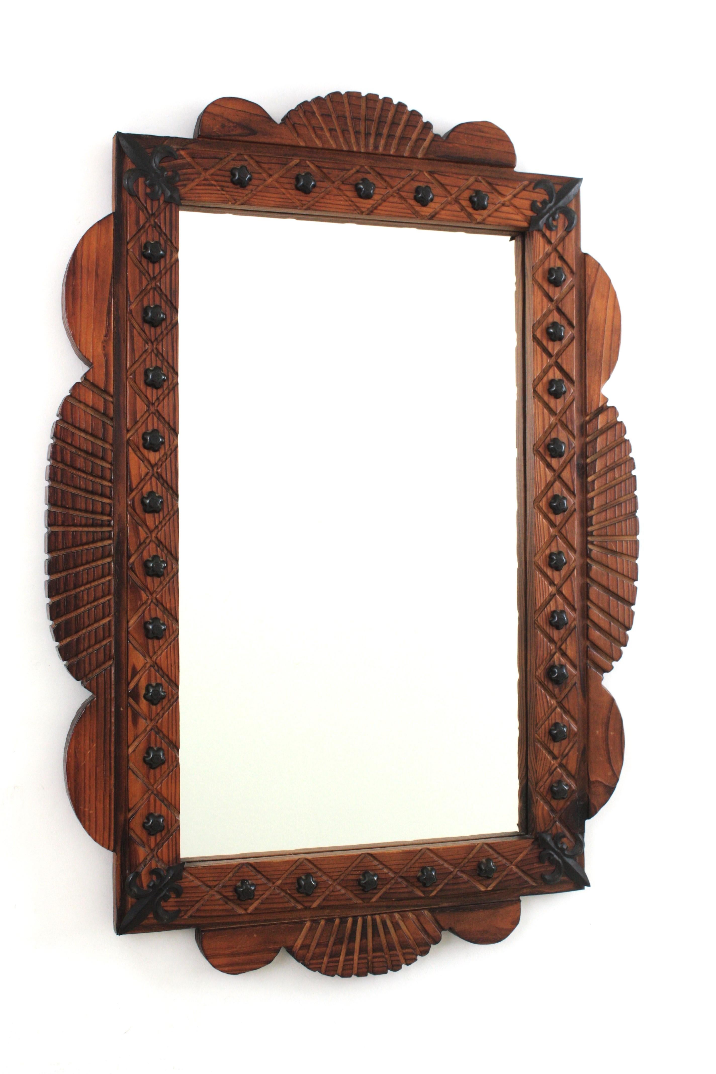 Hand carved pine wood rectangular wall mirror with iron studs and fleur de lis details, Spain, 1940s.
This wall mirror features a wooden rectangular frame with scalloped accents.The frame is adorned by a carved pattern, iron flower shaped studs and