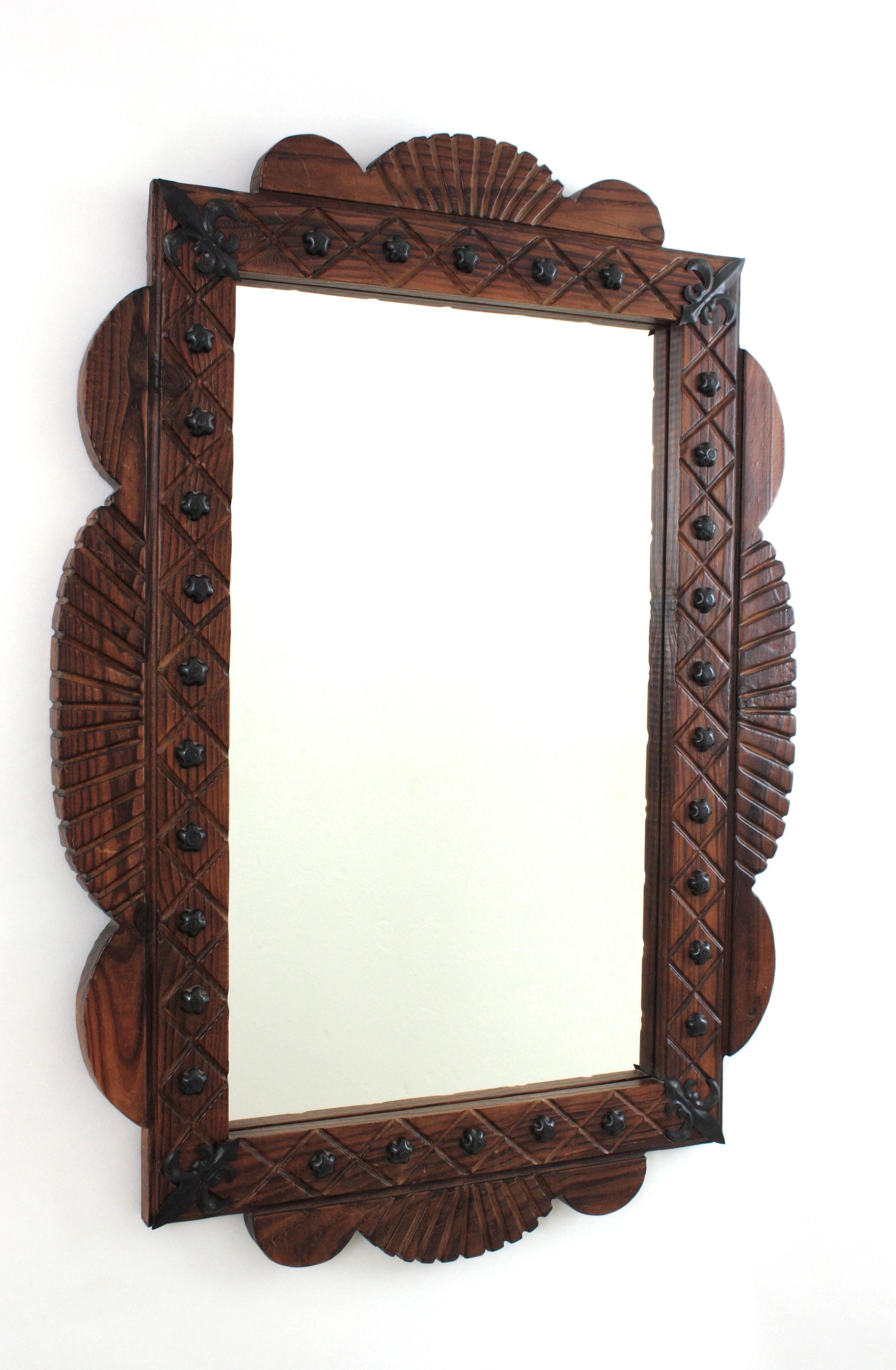 Hand carved pine wood rectangular wall mirror with iron studs and fleur de lis details, Spain, 1940s.
This wall mirror features a wooden rectangular frame with scalloped accents.The frame is adorned by a carved pattern, iron flower shaped studs and