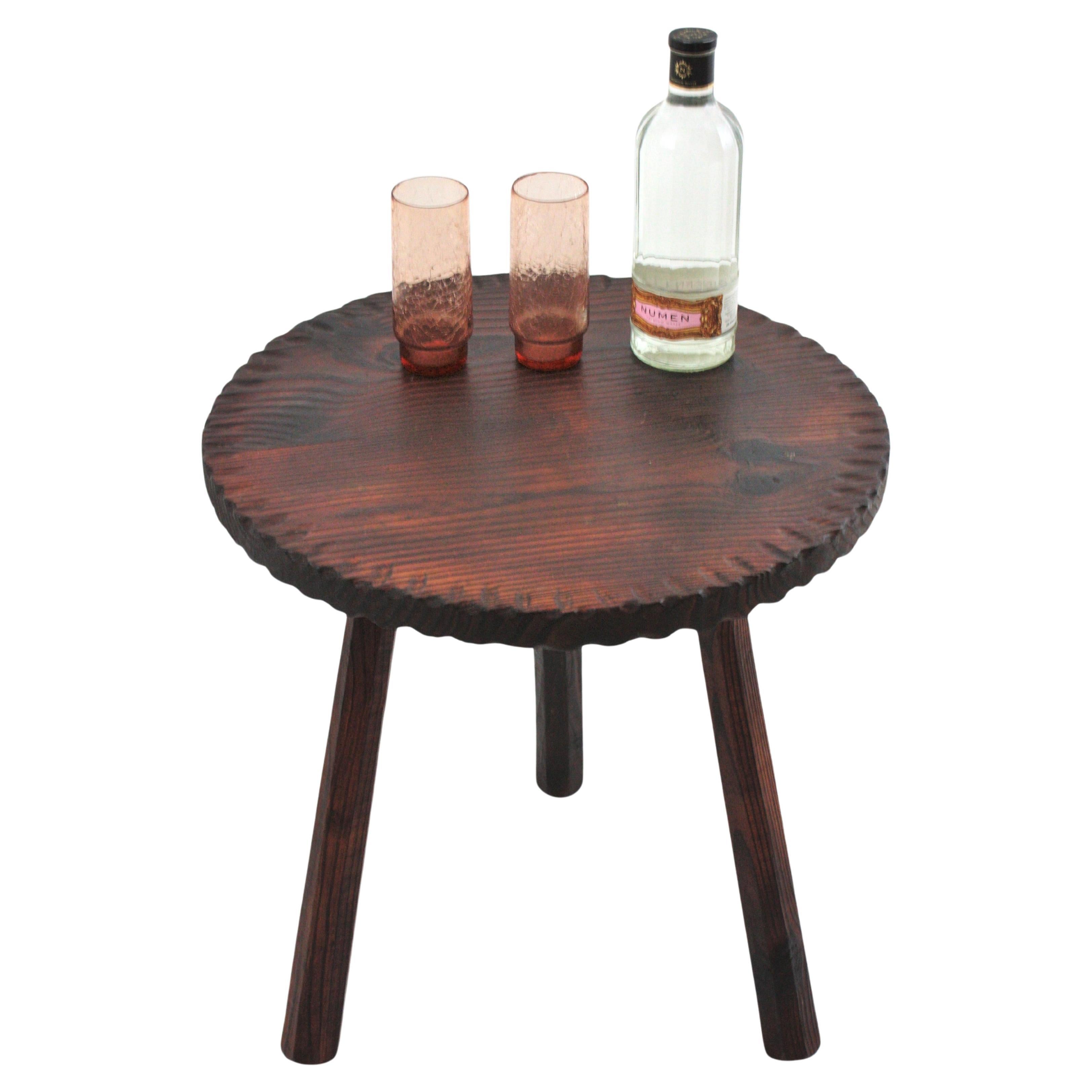 Mesa de gueridón o mesa ocasional de madera de pino tallada a mano y apoyada sobre tres patas. España, años 50.
El tablero de forma redonda tiene detalles tallados y festoneados en el borde. Se apoya en tres patas de madera.
Esta mesa tiene un