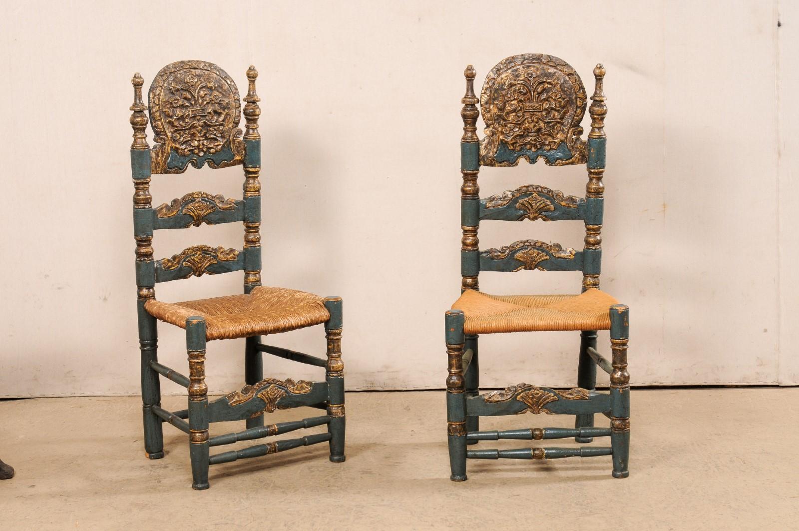 A Spanish pair of Spanish Colonial style, carved and painted wood ladder back chairs with rushed seats. This vintage pair of chairs from Spain, designed in 18th century Spanish Colonial style, have ornately-carved head rests atop a high open and
