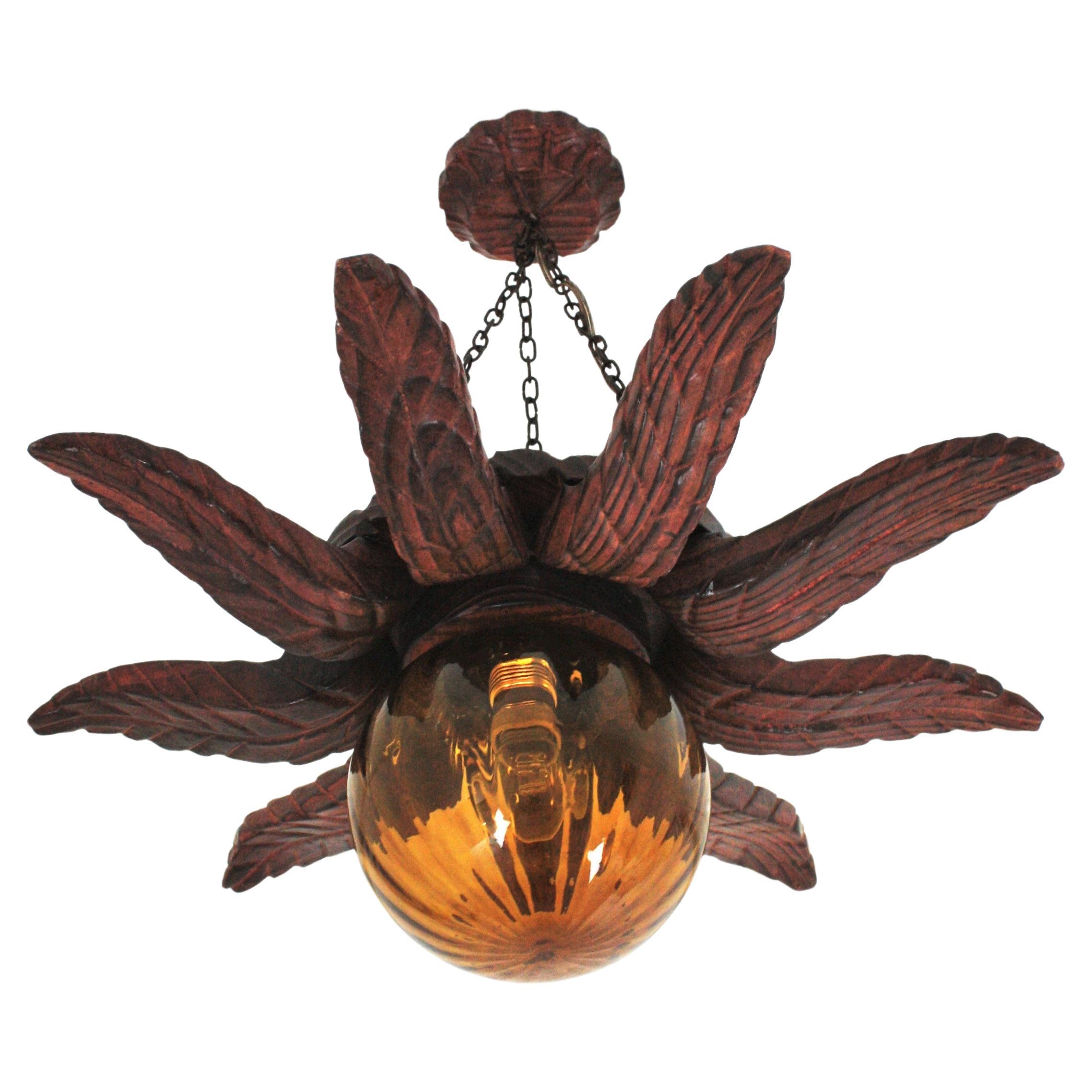 Handcarved pine wood sunburst or starburst ceiling light fixture with amber glass globe lampshade. Spain, 1940s
This ceiling light pendant lamp has an eye-catching construction. The sunburst backplace in carved wood and sunburst or starburst shape