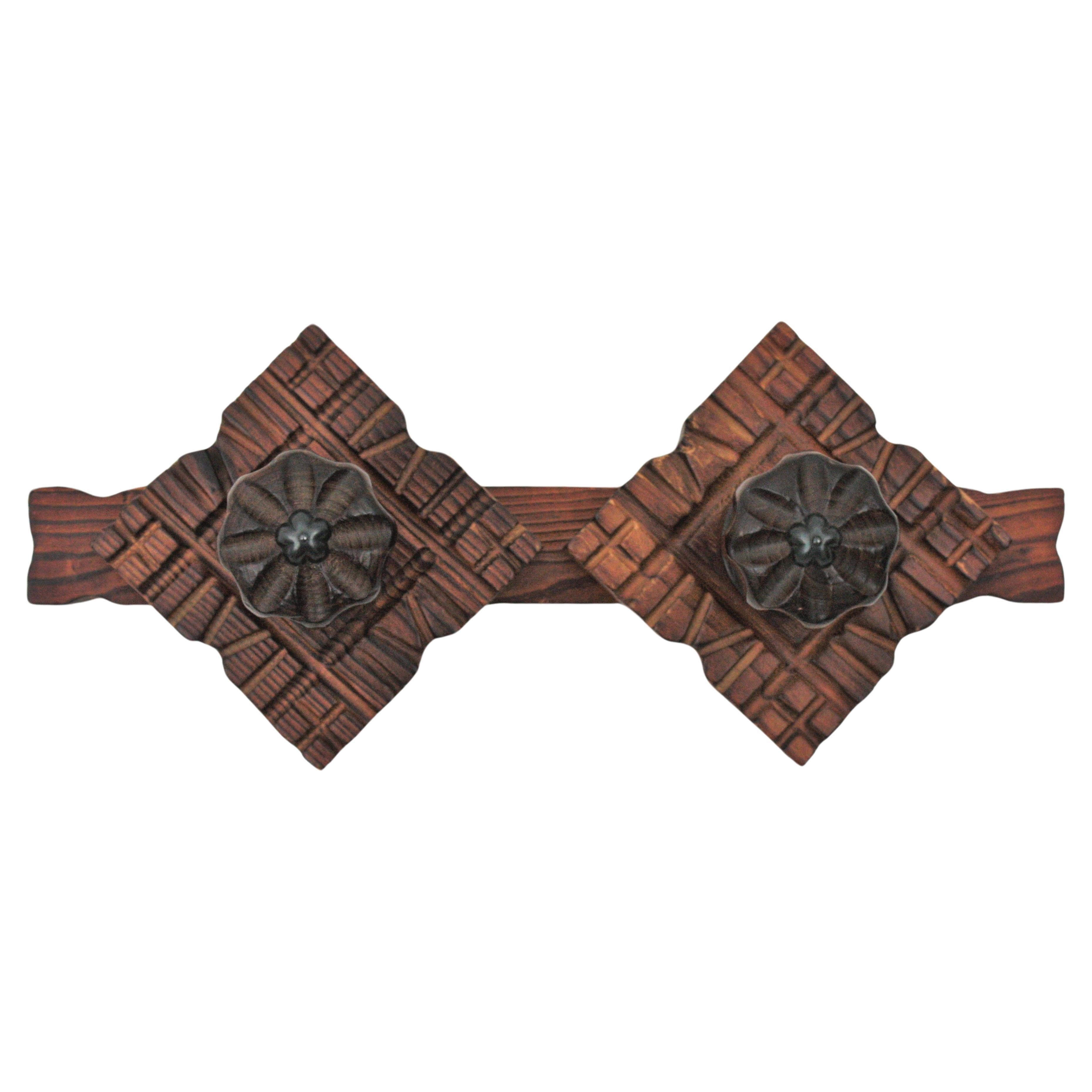Handcarved pine wood wall coat rack, 2 hangers, Spain, 1940s.
This eye-catching coat rack has 2 flower shaped hangers with beautifully carved and rhombus shaped backplates with geometric details.
It has a rustic finish and spanish colonial