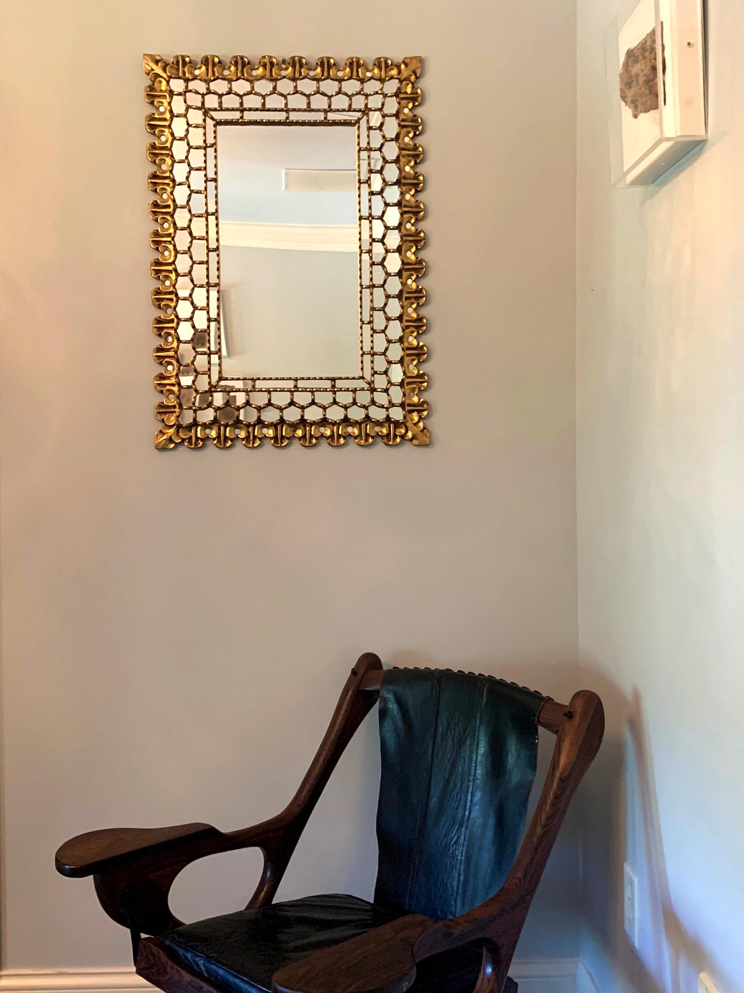 Miroir mural en bois sculpté d'origine Coloni espagnole, fin du 19e siècle ou début du 20e siècle.
Le cadre doré a été sculpté dans du bois massif et présente des motifs de fleurs de lys dans les coins et trois anneaux de panneaux miroirs complexes
