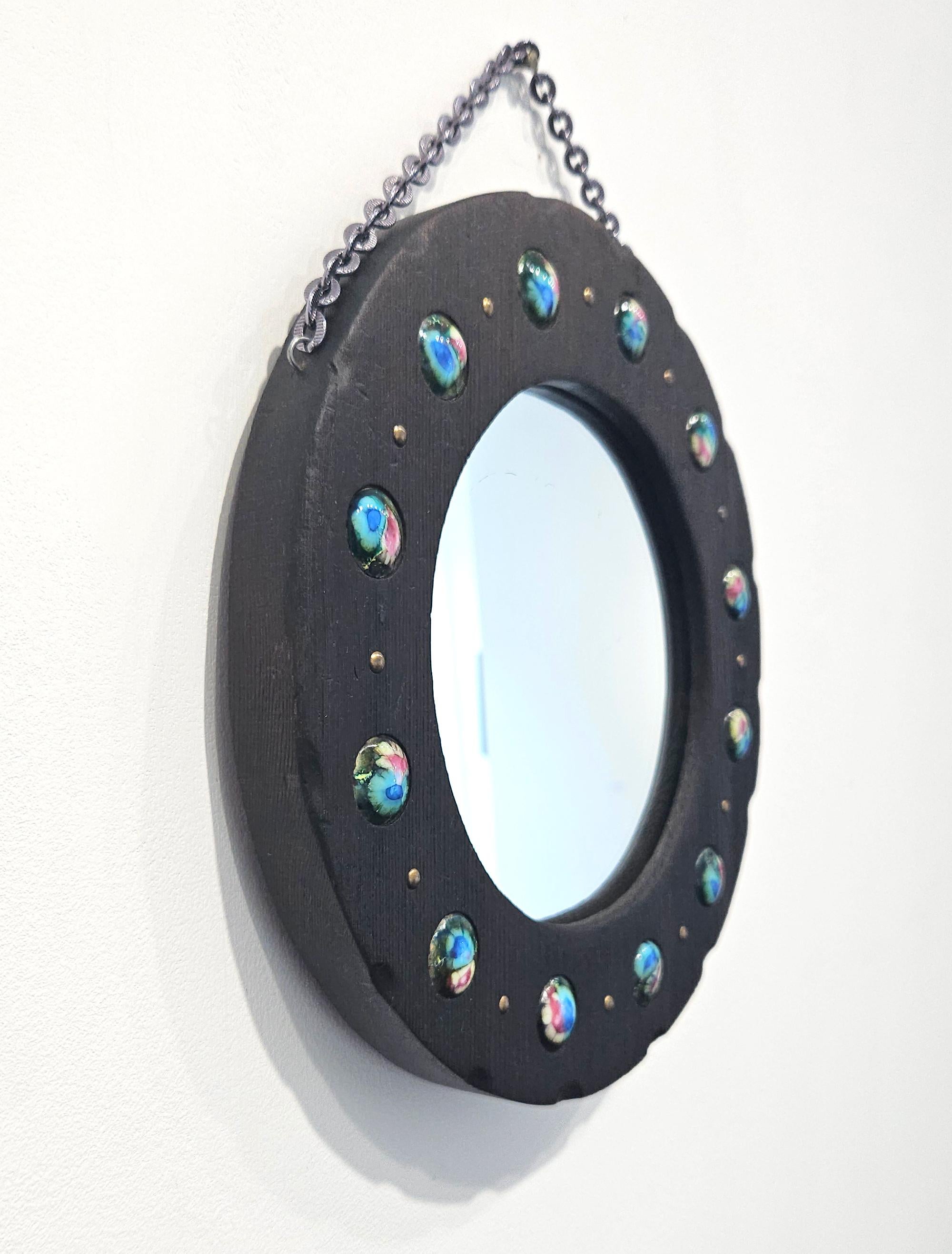 Charmant et inhabituel petit miroir circulaire en bois du milieu du siècle avec des détails en émail coloré, fabriqué par Capo Esmaltes en Espagne vers 1960. 

Le cadre circulaire en bois sombre sculpté à la main est orné d'une série de douze