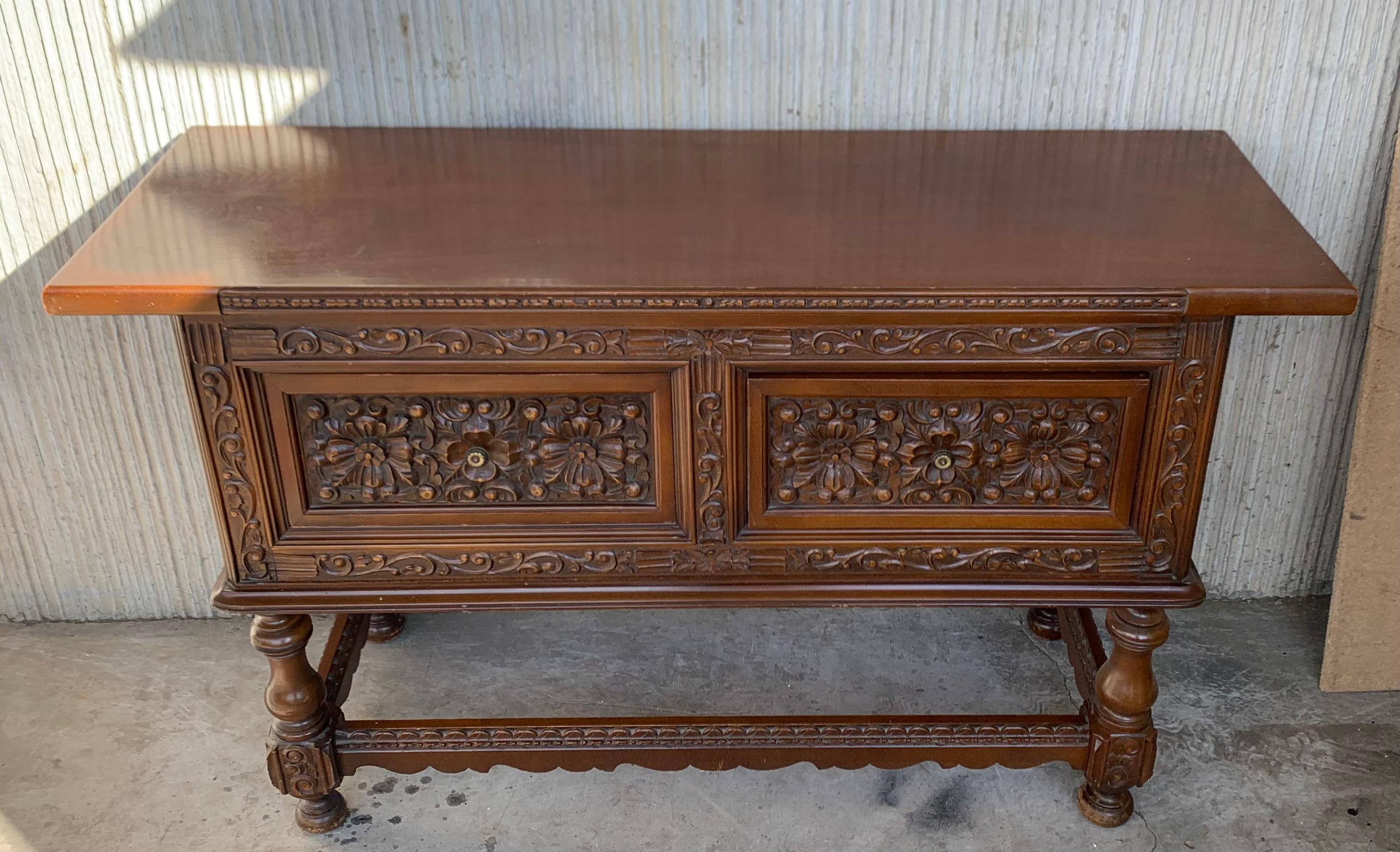 This large Spanish early 20th century features a beautiful one plank rectangular top over two wide carved drawers. Each drawer, featuring slightly different hardware, is adorned with floral motifs. Rosettes are carved between the drawers and each