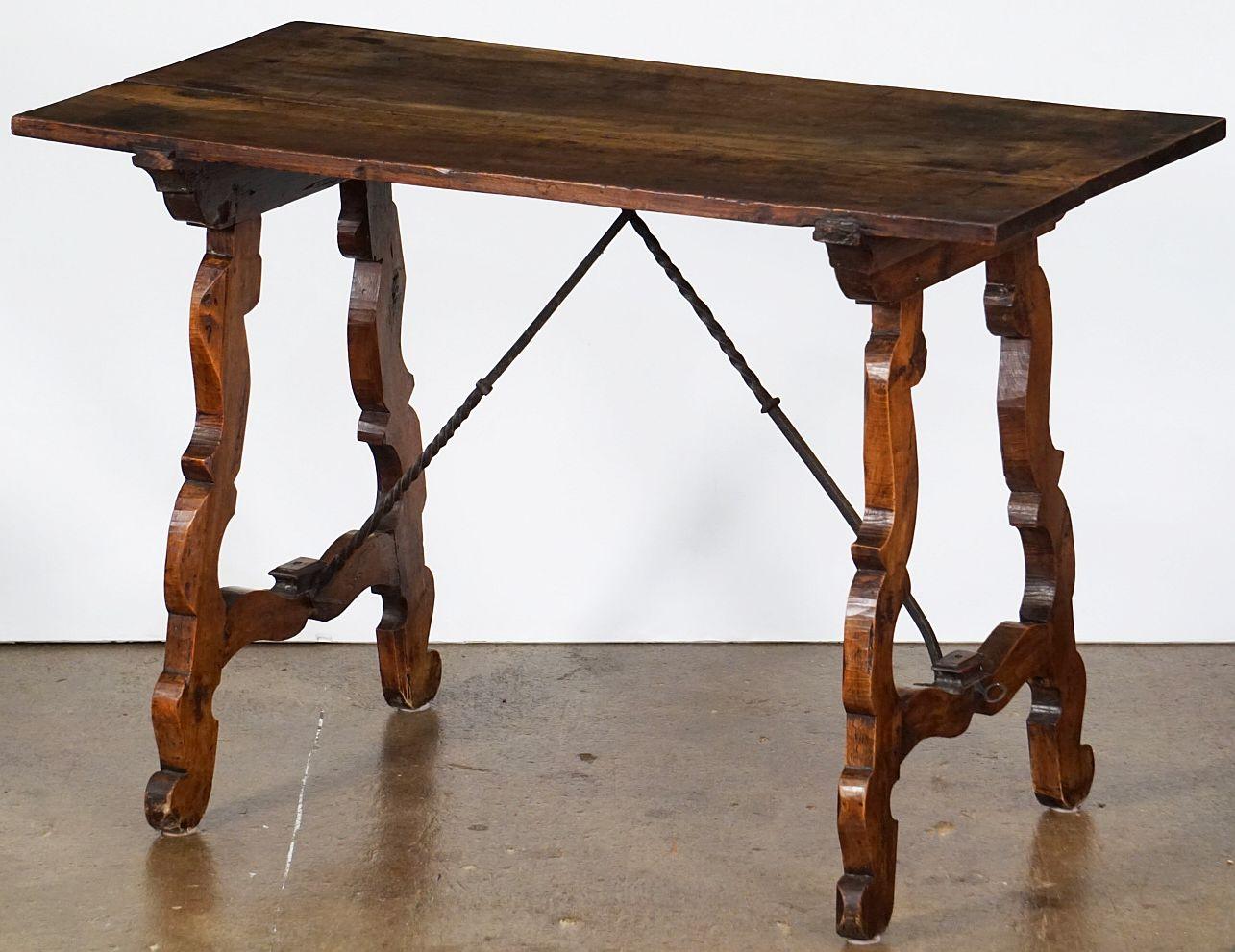 A fine Spanish console or trestle table of patinated walnut, in the rustic Baroque style, featuring a rectangular plank top over a frieze of two turned serpentine wood supports with wrought ironwork braces in a cross-bar design.