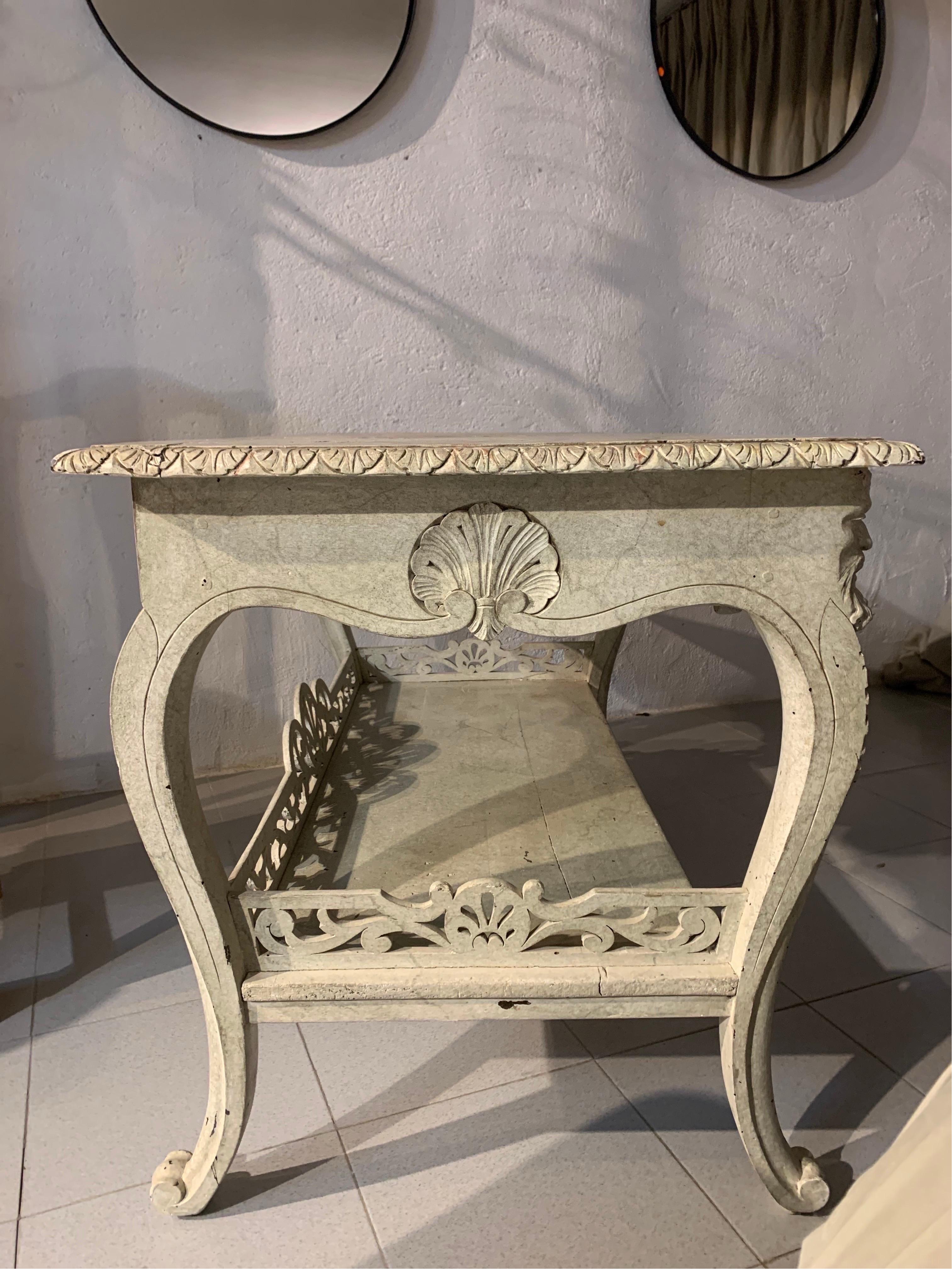 A rare Spanish console table, in hand-carved and bleached wood, with a top in wood imitating marble, hoof-shaped legs, which at the top end in two carved heads that act as a base for the hand-painted top imitating marble. They have a shelf at the