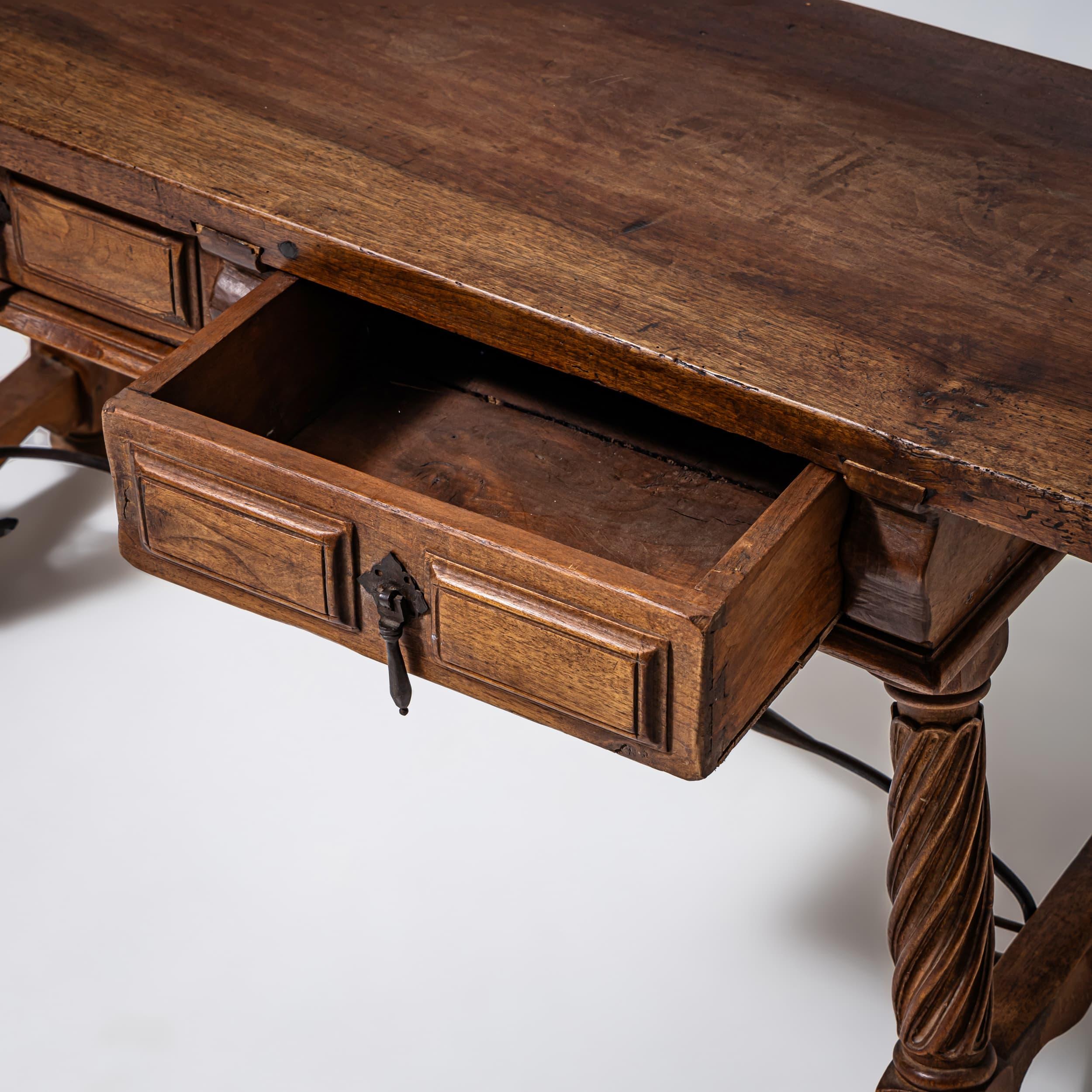 Spanish table or bench with a height of 54 cm. The piece rests on baluster legs with twisted shafts and an iron stretcher. The apron features two drawers with iron pulls.
