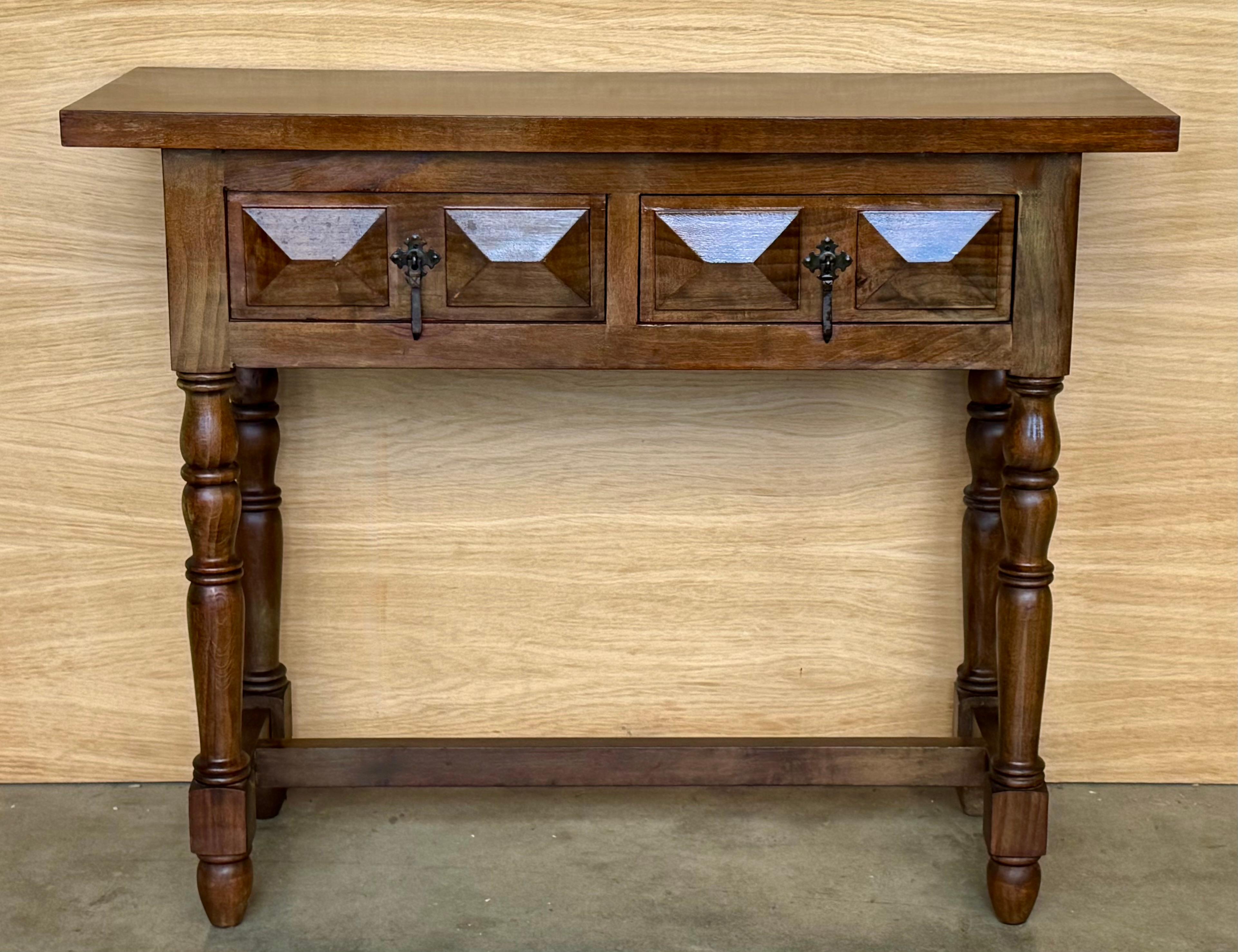 Spanish console table with two carved drawers, with iron handles that stand on four legs in the shape of domed columns and in turn carved with straight lines. These four legs are joined by an arched wooden fastener.


