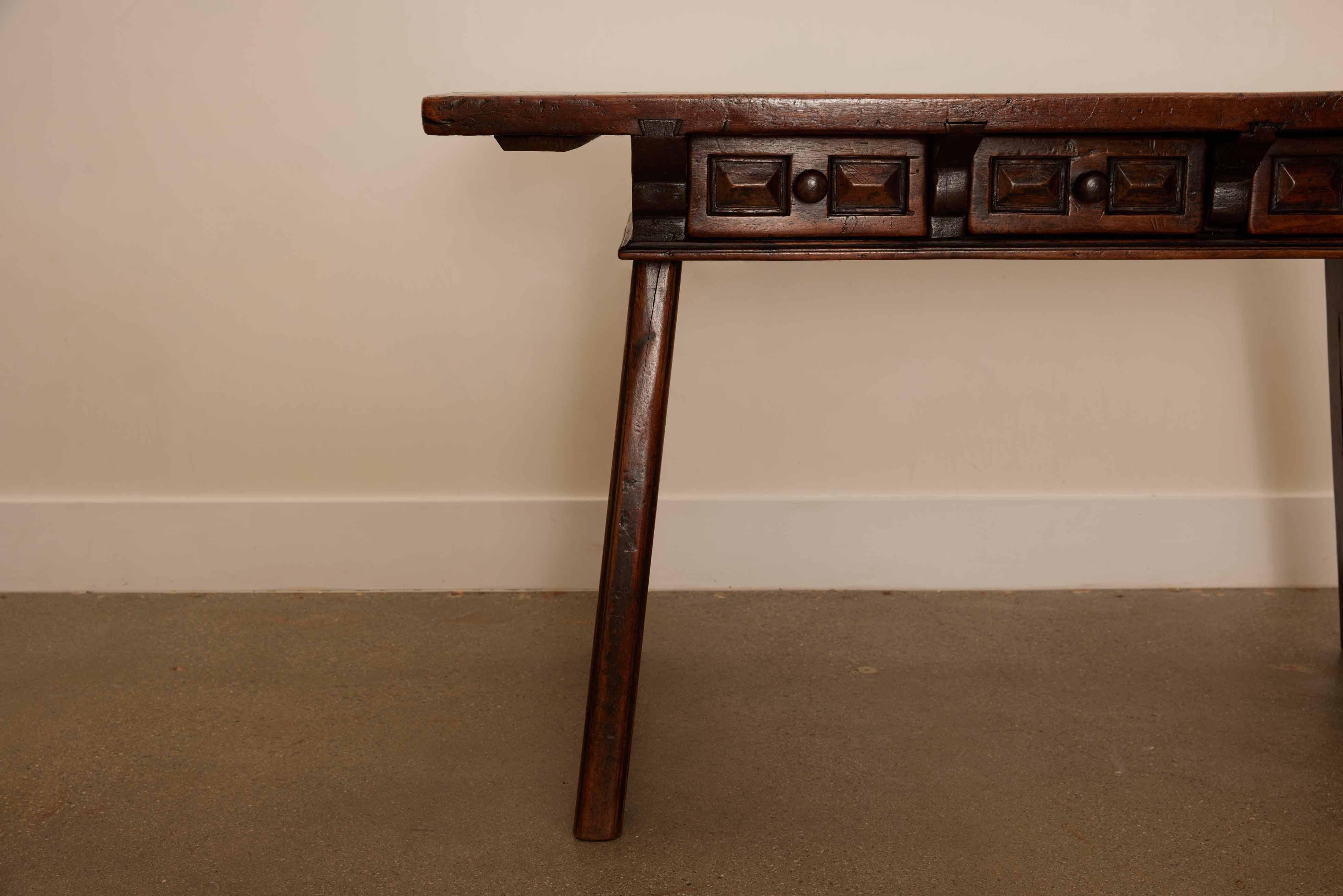 This 18th-century Spanish console table that has three exquisite hand carved drawers with geometric detail.  The table stands on robust trestle-style legs, connected by elegantly carved side stretchers for added stability and aesthetic appeal.