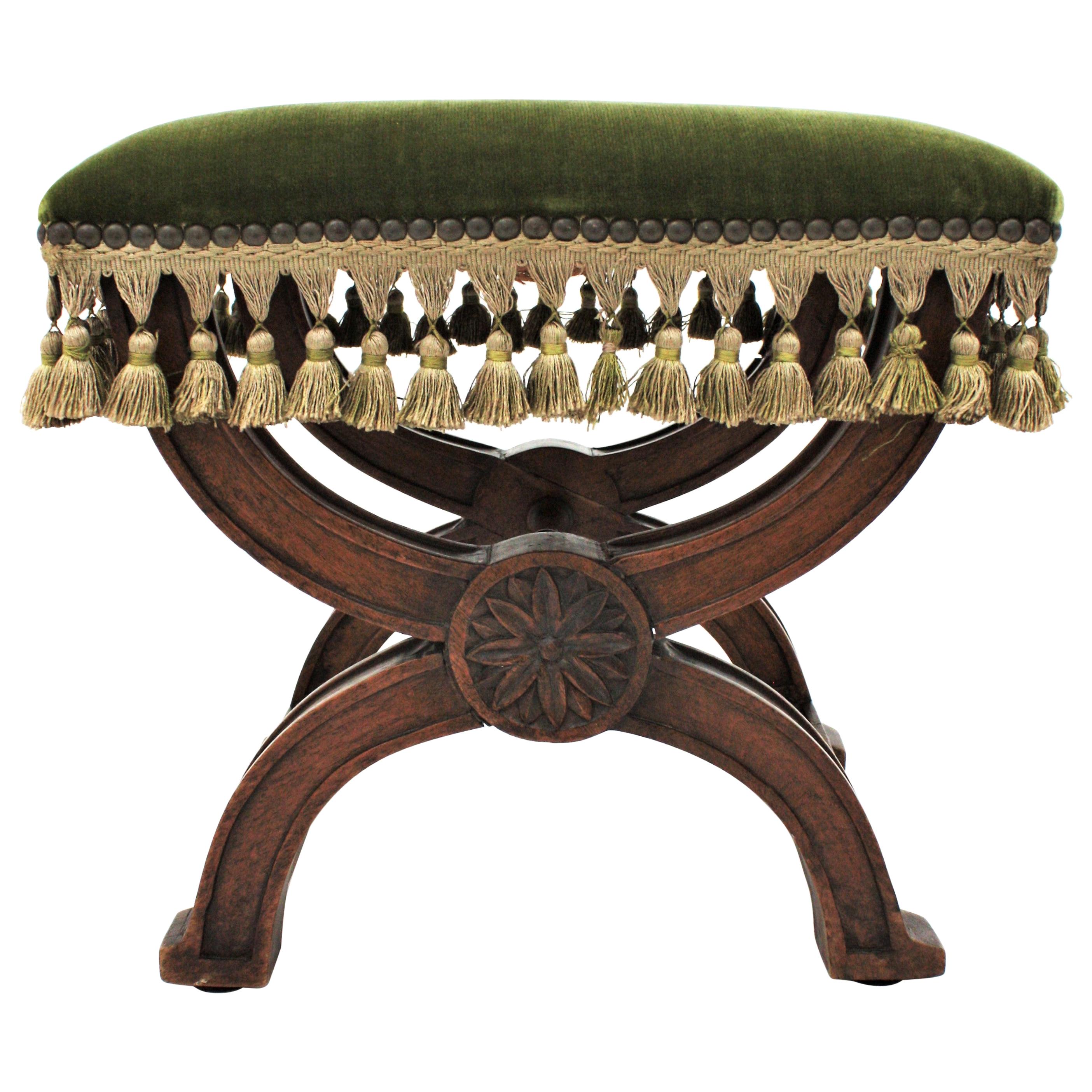 Spanish Renaissance Curule walnut stool in green velvet upholstery, Spain, 1880s.
Elegant Curule X-shape carved walnut footstool /ottoman with green velvet upholstered fringed seat.
This finely carved small stool has decorative floral ornaments on