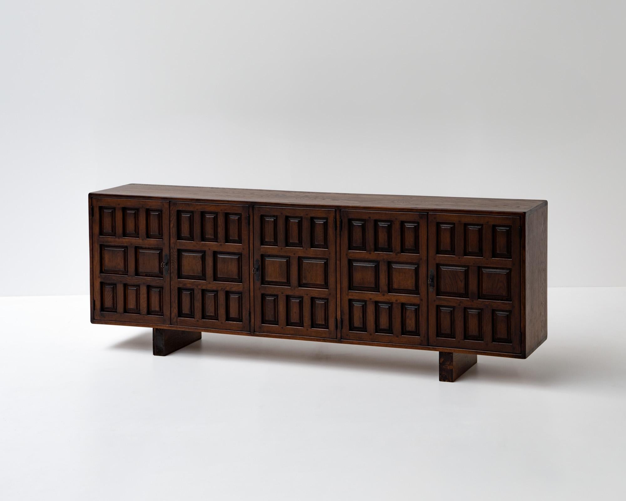 This is an exceptional Spanish brutalist sideboard with intricately carved squares on the door panels. Its dark stained wood finish gives it a sophisticated look that complements various interior styles. 

With a subtle nod to the iconic Biosca