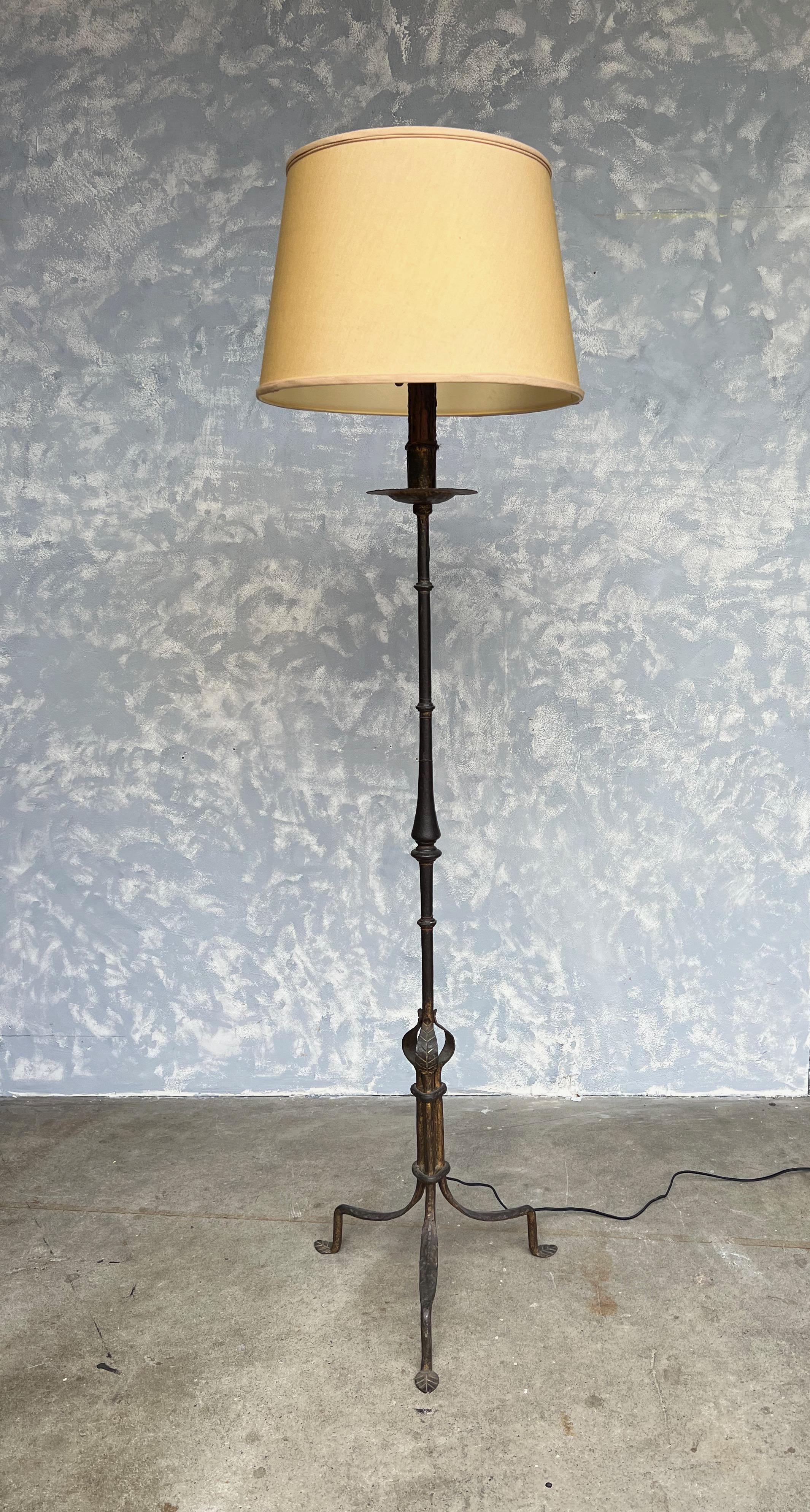 Presenting an extraordinary Spanish 1950s gilt iron floor lamp resting on an elevated tripod base. This lamp boasts a beautifully aged dark gold patina and a stunning hand-hammered texture, creating a captivating visual appeal. The upper part of the
