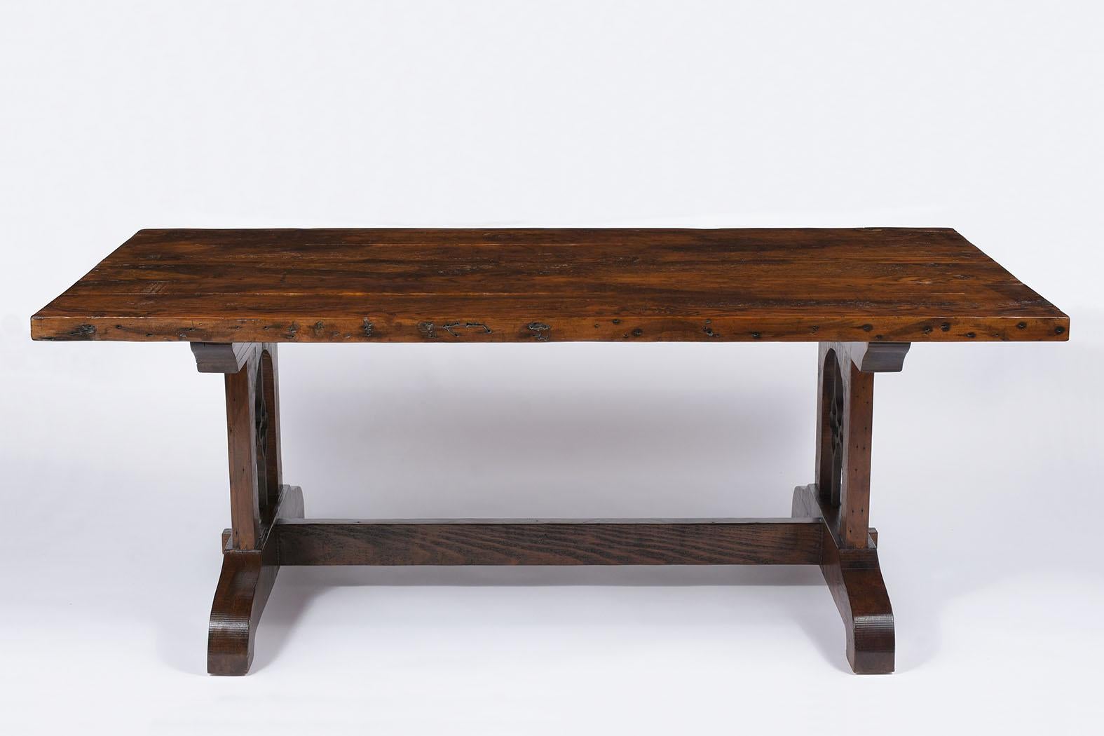 This exceptional Spanish Colonial style dining table made out of solid pine wood features a new rich walnut finish with a clear waxed varnish and polished patina finish. The table has a rectangular wooden top raised by stretched pedestal legs with