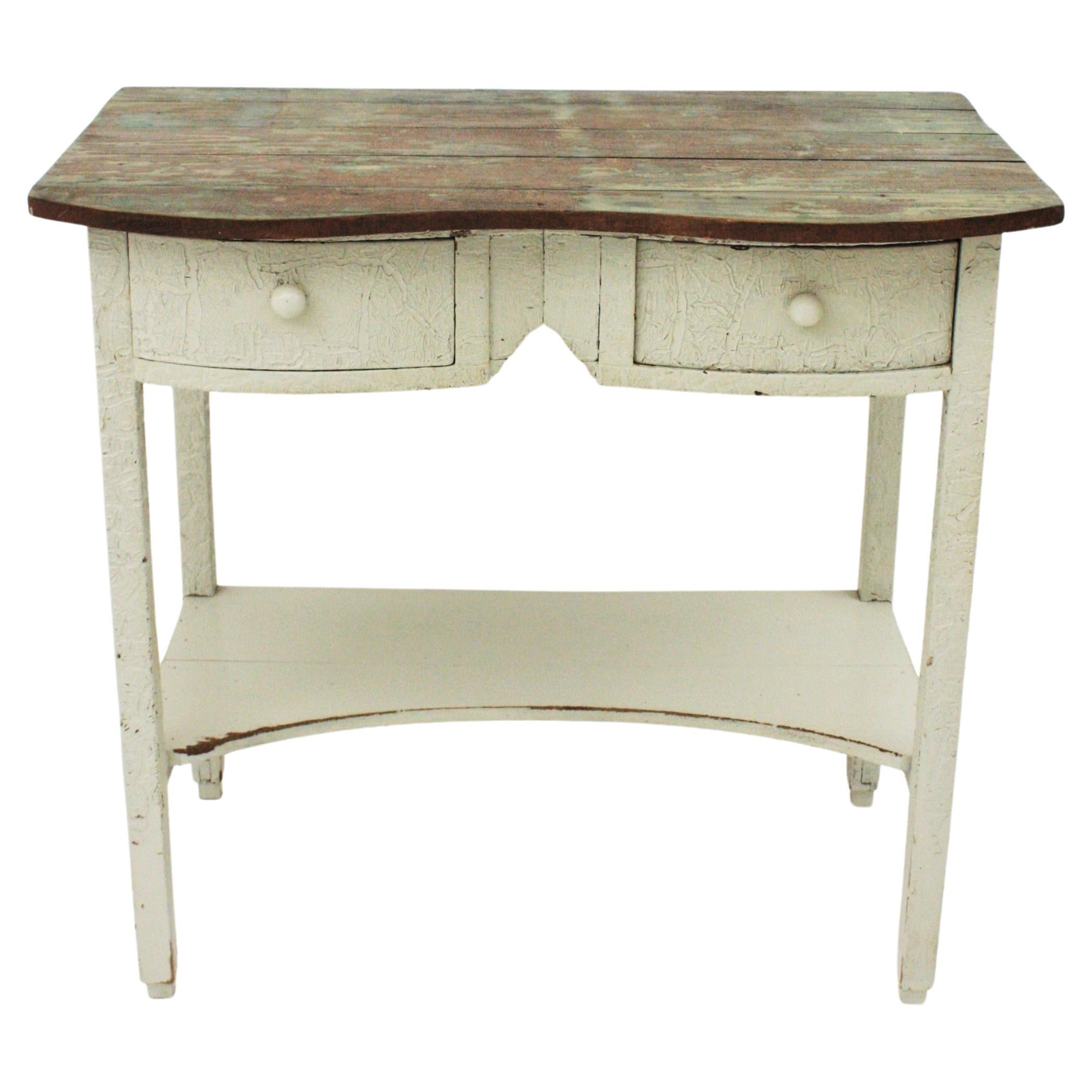 Early 20th century Spanish rustic off-white painted pine farm kitchen table or occasional table.
Charming pinewood Spanish farmhouse or kitchen table with two drawers and a lower shelf. The bottom part is patinated in off white with a cracked