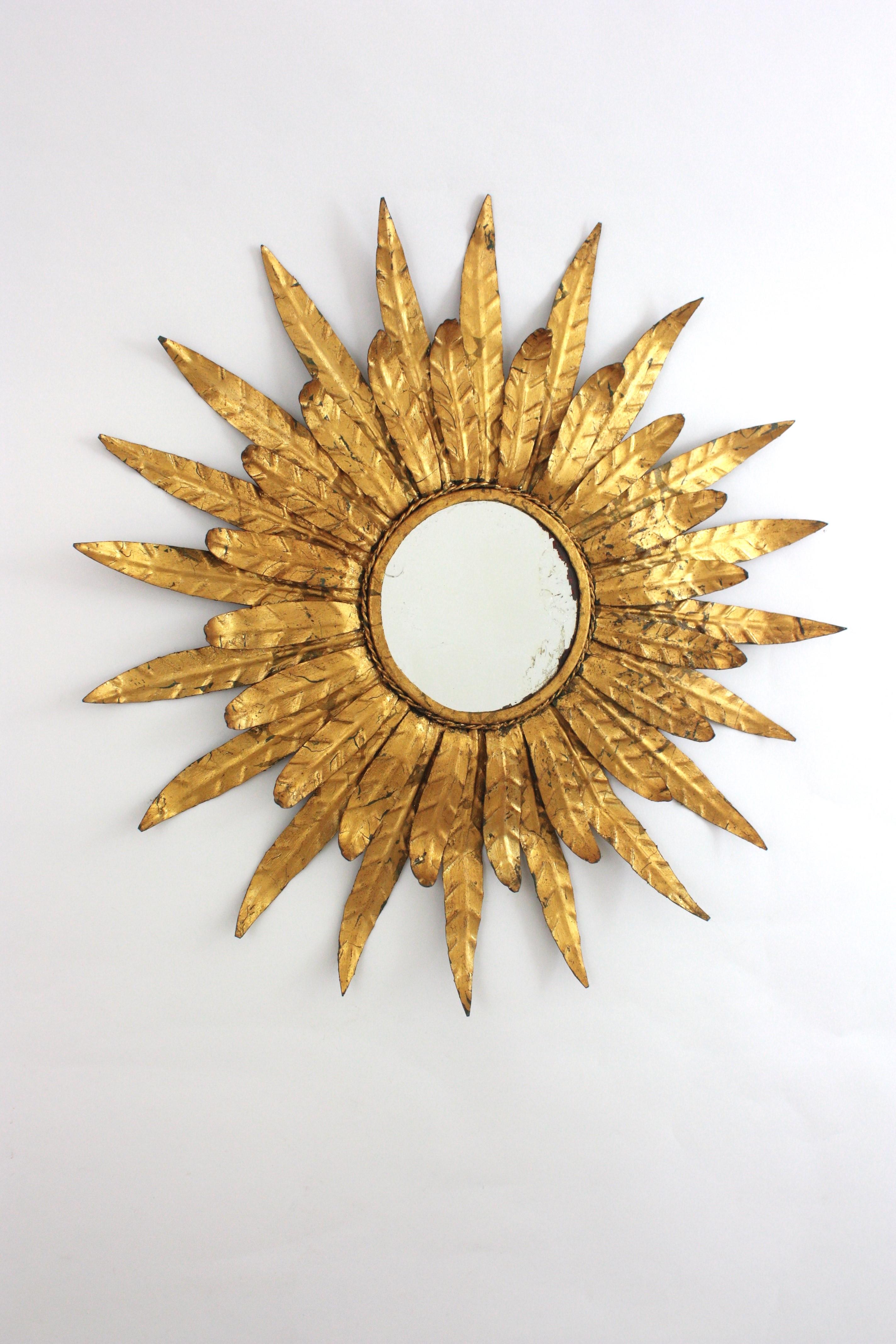 Specchio a raggiera incorniciato con foglie, ferro dorato Spagna, anni 1950-1960.
Un accattivante specchio a raggiera incorniciato da due strati di foglie grandi e piccole che circondano un vetro rotondo centrale. Splendida patina invecchiata e