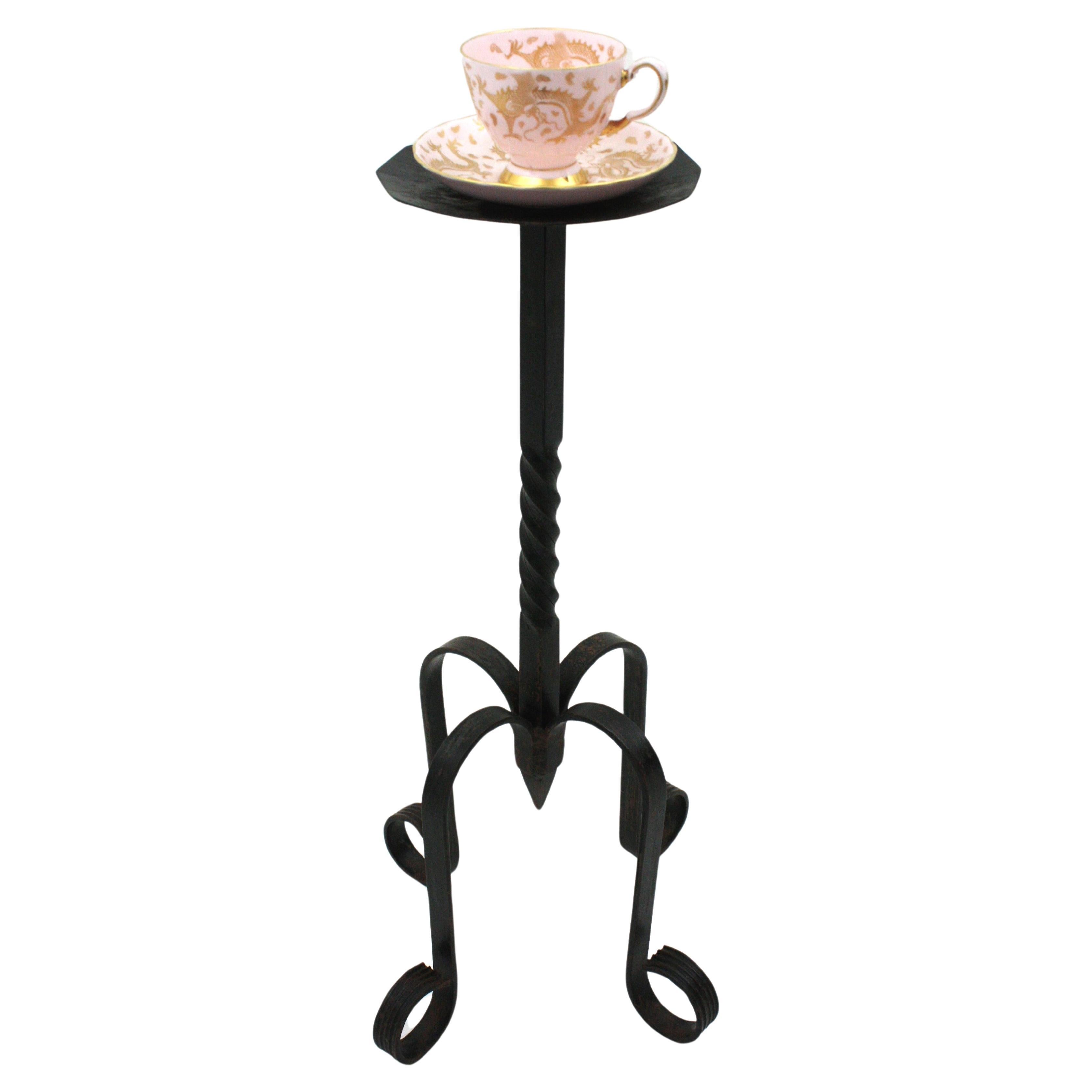 Elegant Gothic style hand-hammered iron round gueridon table standing on a tripod base. Spain, 1940s.
This wrought iron black painted table has twisted details at the steam and the top stands on a four footed base with scroll endings on each